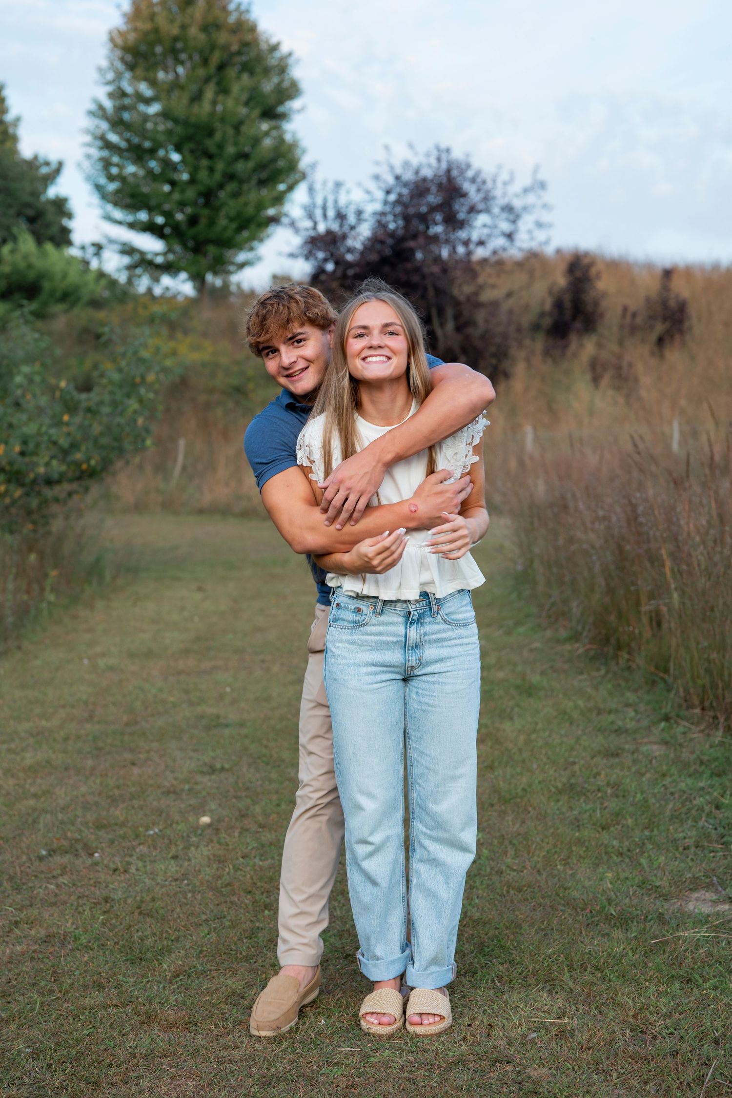 Couple embracing and laughing together in a field during golden hour.