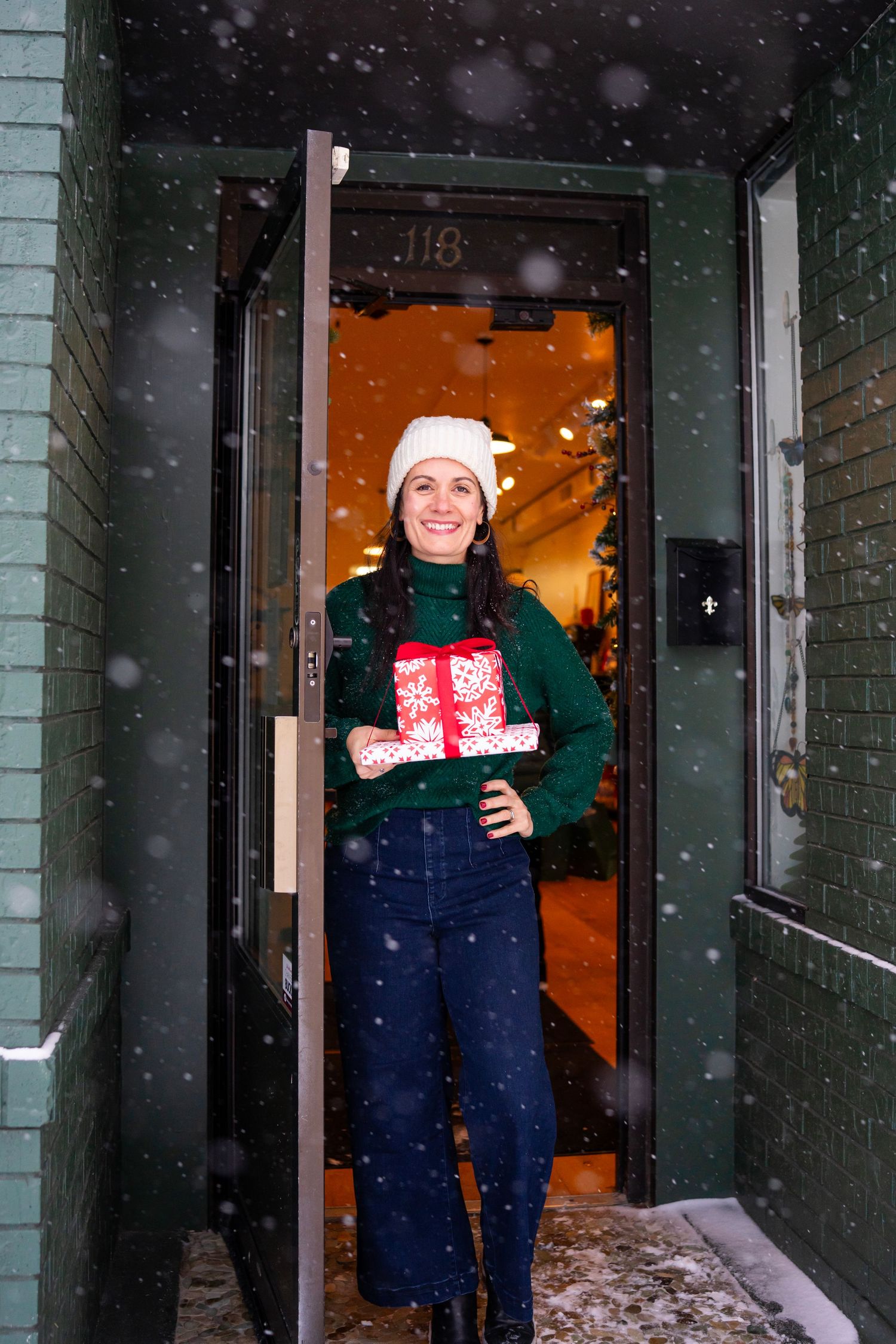 Snowy entrance to a business with holiday decorations and green brick exterior.