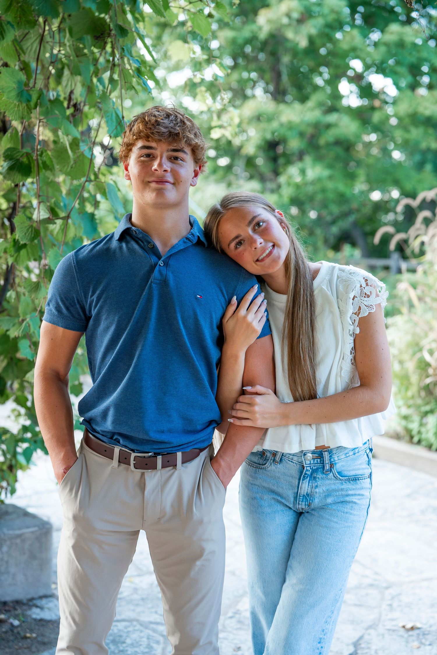 A couple posing together under green leafy vines in summer.