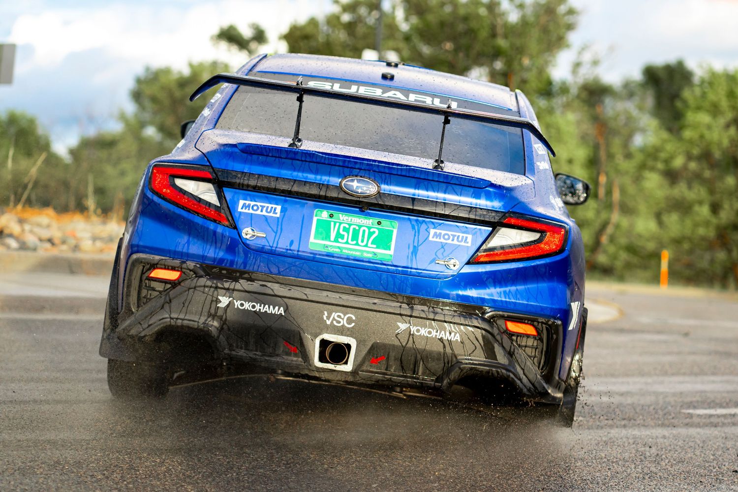 Blue rally car drifting through corner showing aggressive racing stance.