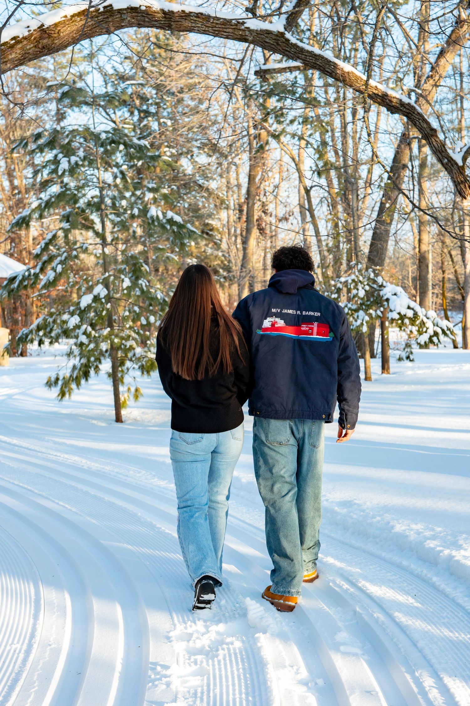 Two people walking together through a snowy winter forest path with groomed cross-country ski trails.
