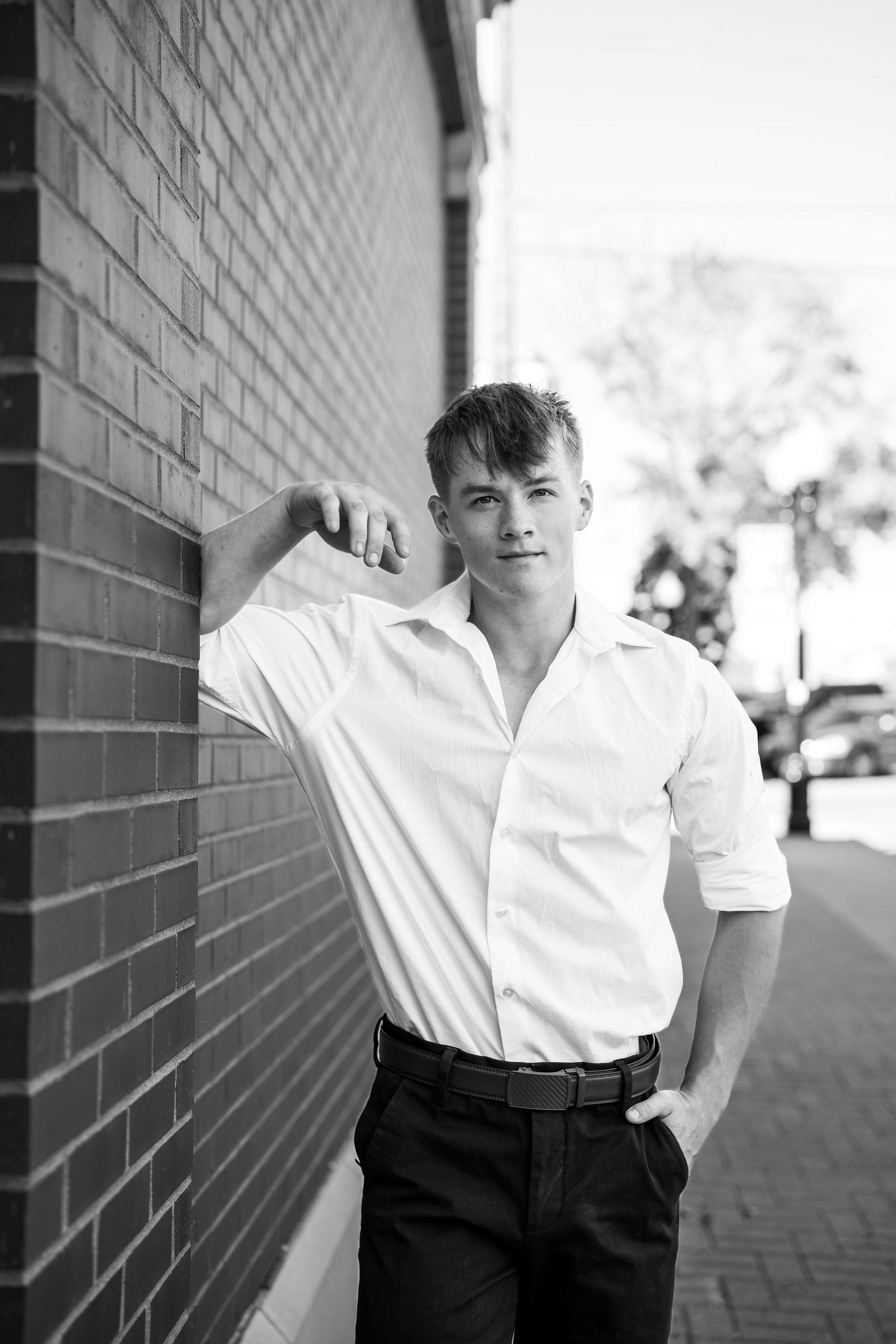 Fashion portraits in white shirt and dark pants against a brick wall with dramatic lighting.