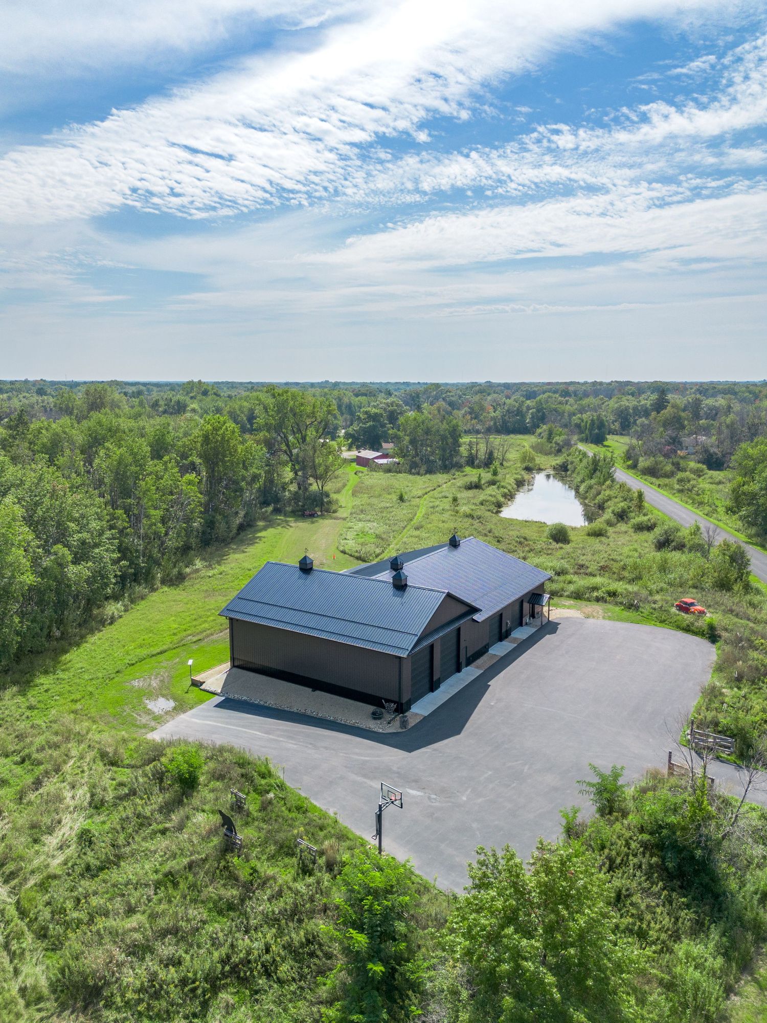 Drone shot of large commercial buildings with solar panels and parking areas surrounded by woodland.