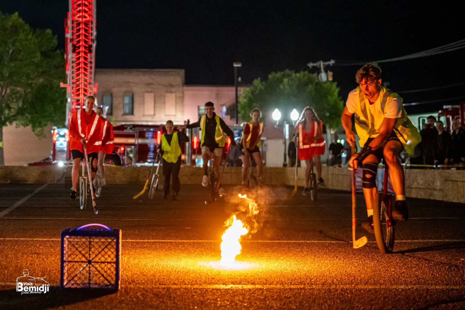 Fire performers on unicycles creating dramatic displays on a dark outdoor course.