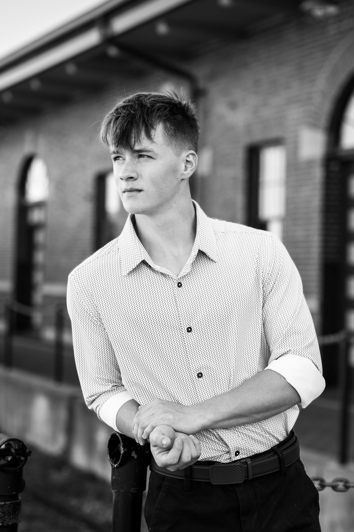 Black and white portrait in striped button-down shirt against brick building exterior.