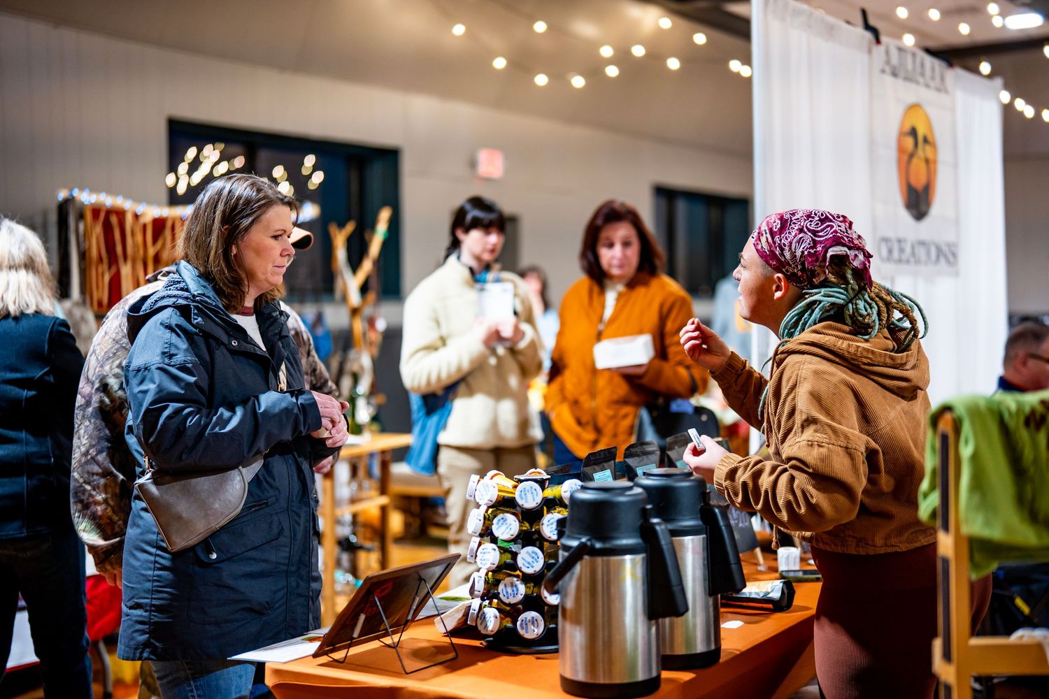 Cozy marketplace interior with string lights and customers enjoying tea samples.