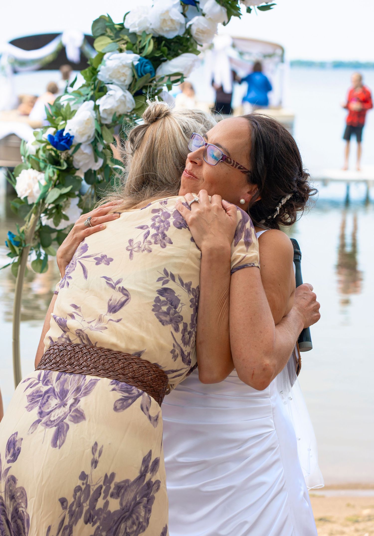 Emotional embrace under floral arch during beach wedding celebration.