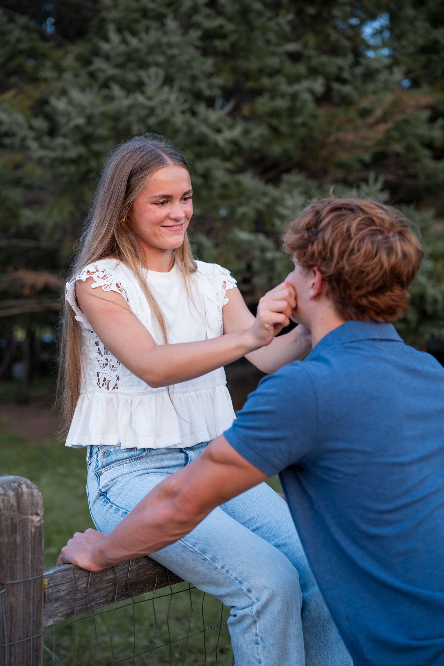A couple shares a playful moment while sitting on a wooden fence.