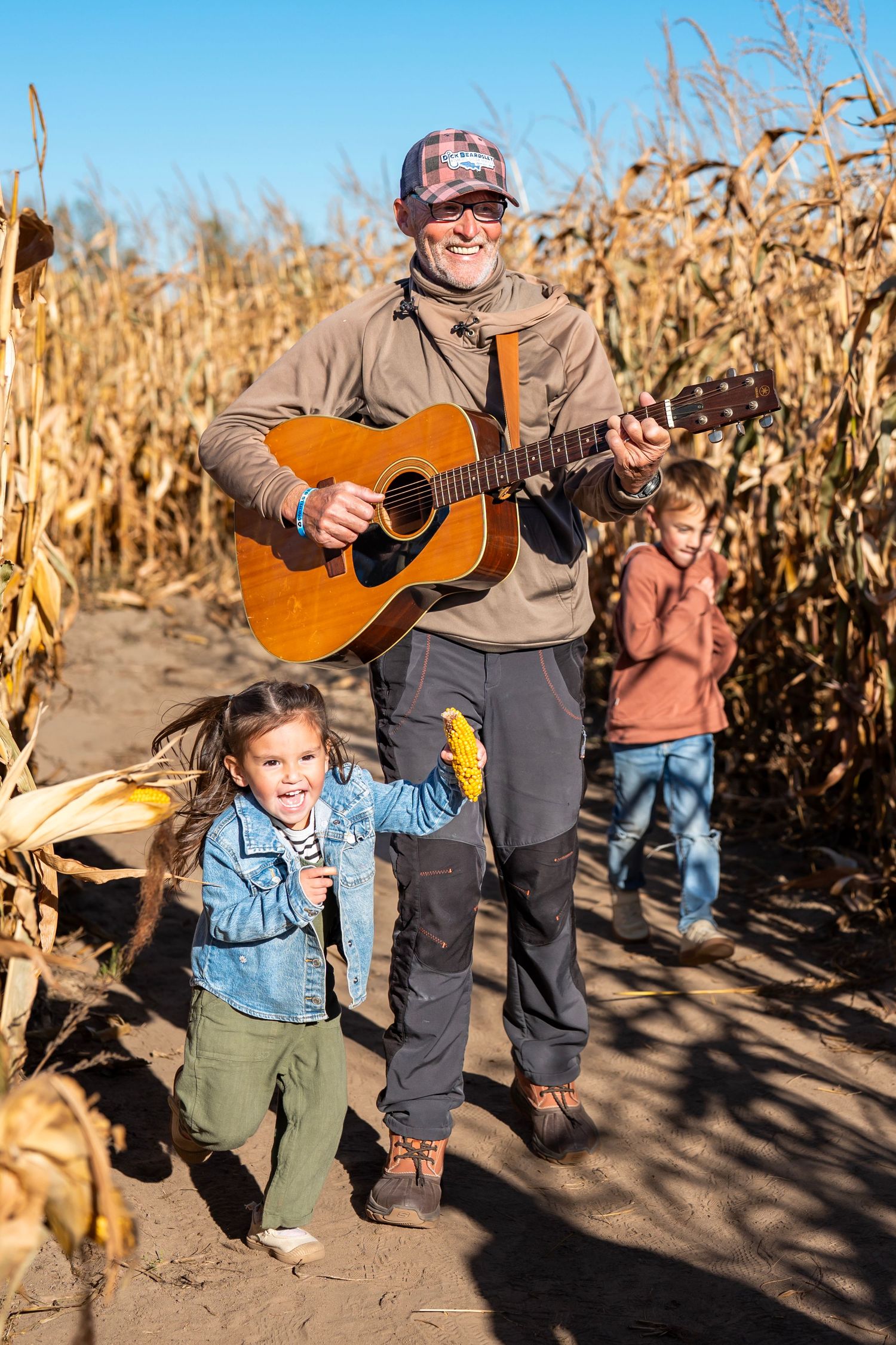 A heartwarming scene of guitar playing and children running among dried corn stalks at sunset.