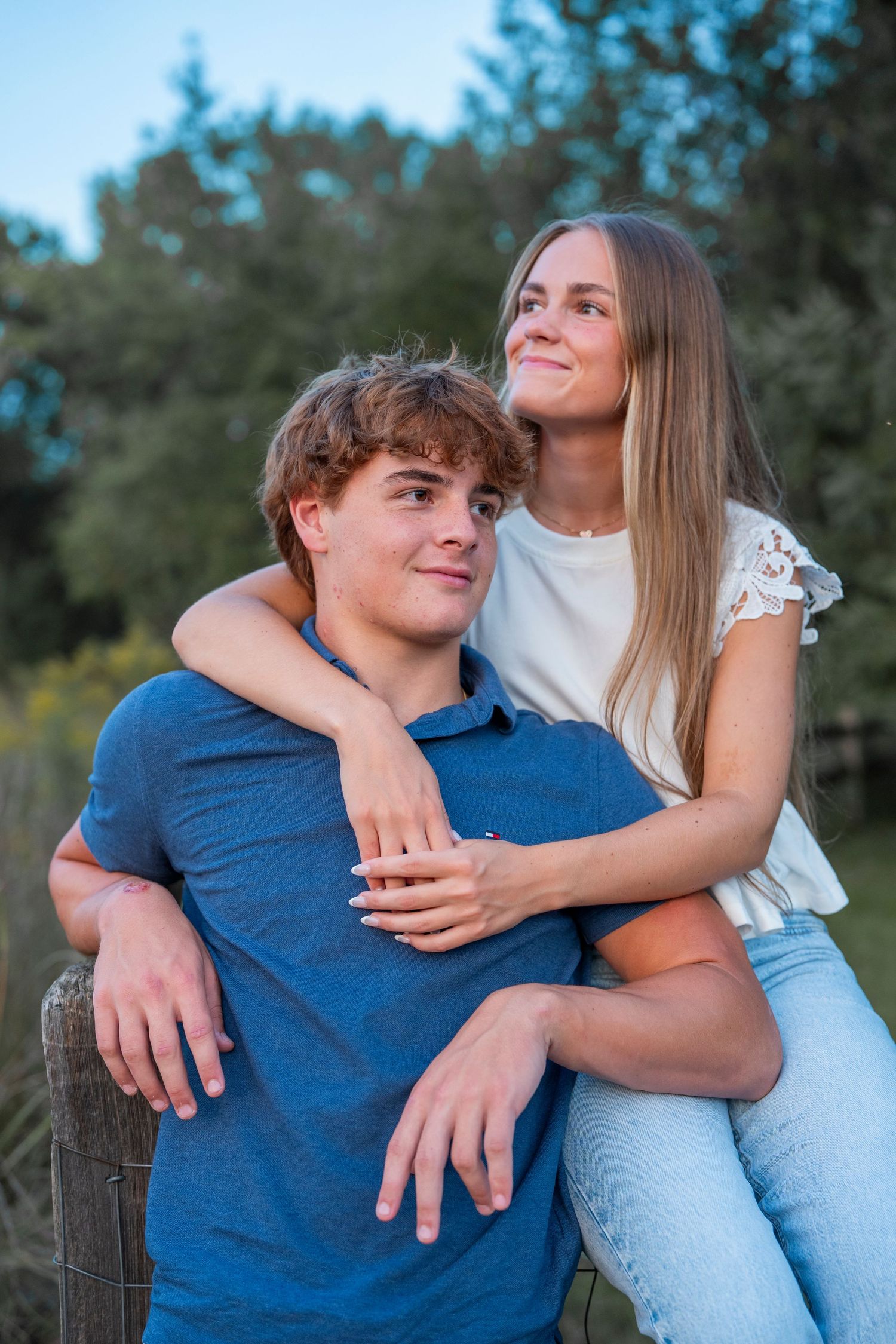 A couple embraces while standing by a wooden fence during golden hour.