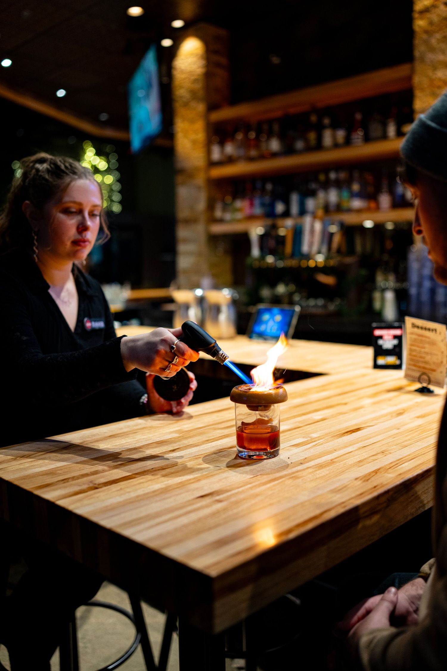 Wooden bar counter with drinks and ambient lighting in a cozy restaurant setting.