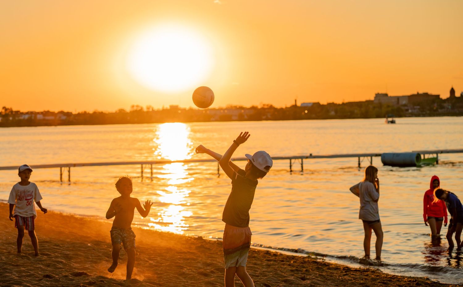 Silhouettes of beachgoers playing games and enjoying leisure activities during a vibrant sunset.