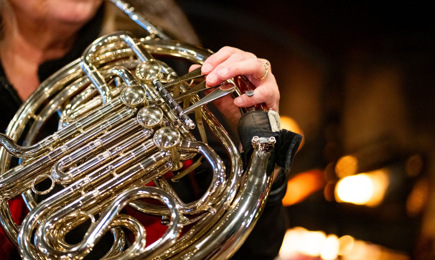 Close-up of hands playing brass instruments in front of a fireplace.