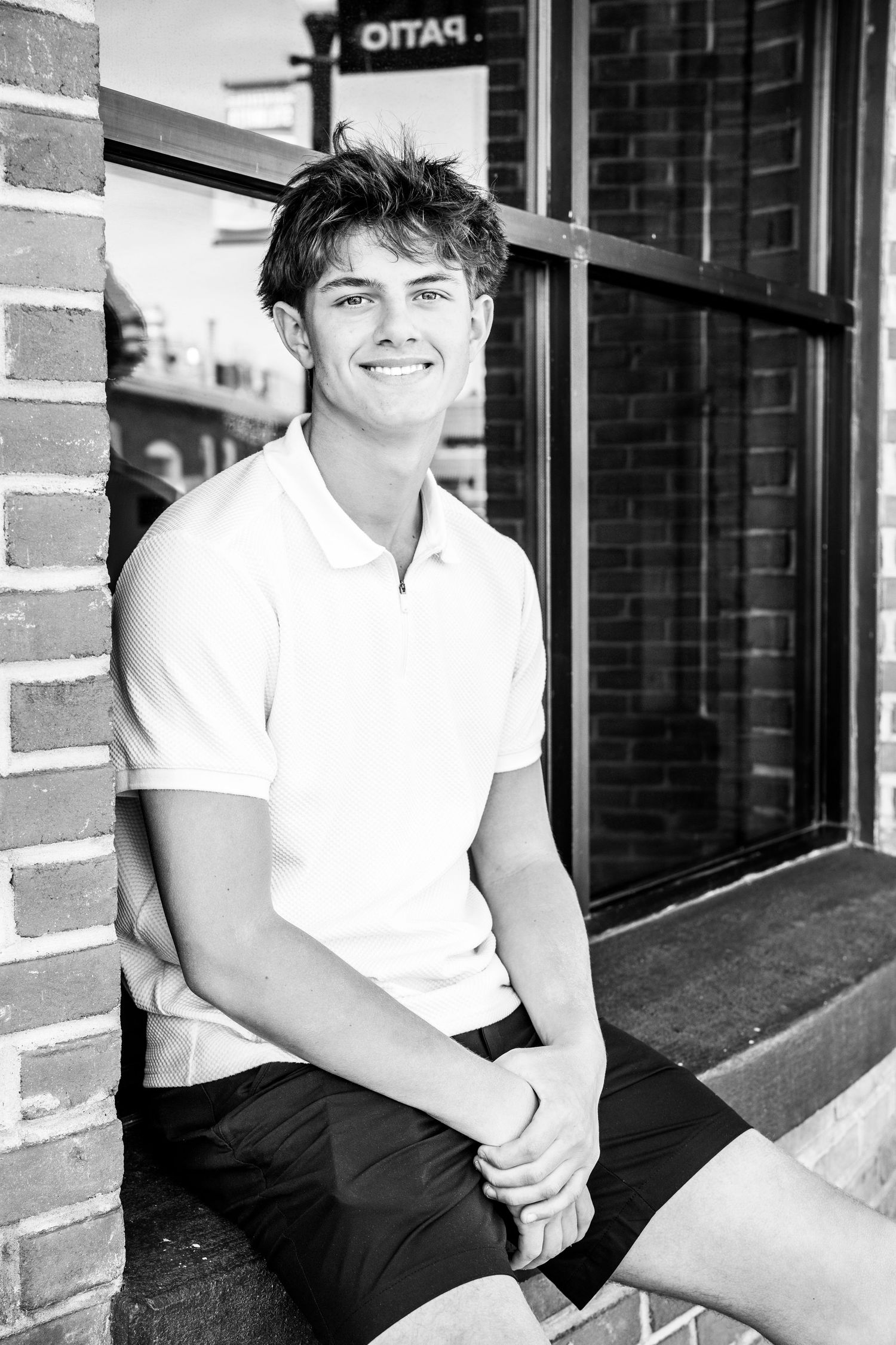 A person in a white polo shirt sits casually on a brick porch in black and white photography.