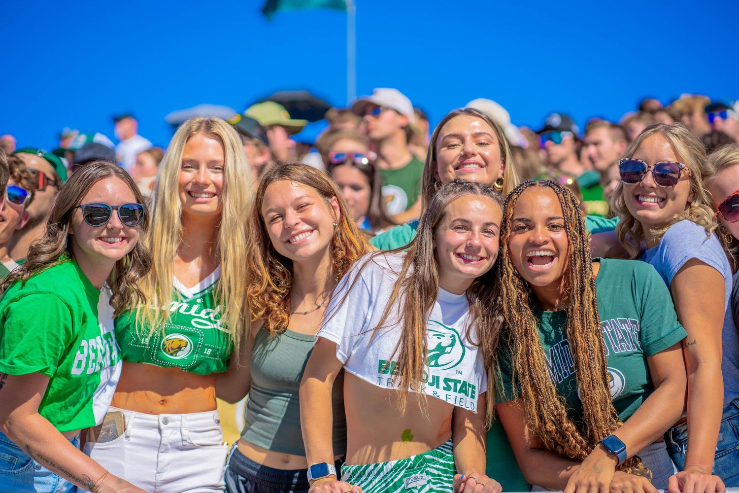 Students in green attire cheering from stadium bleachers during sporting event.