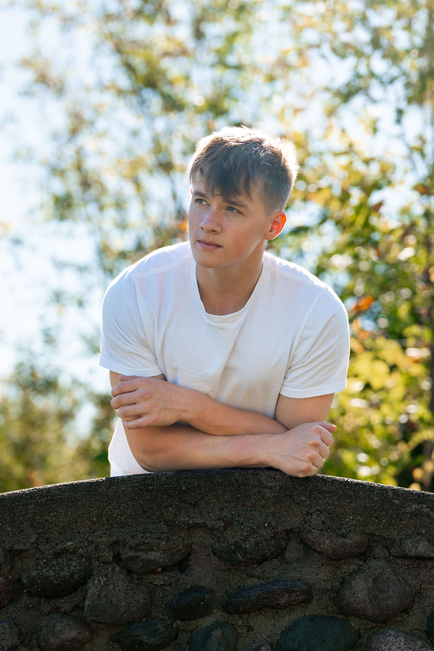 Person in white t-shirt lying on stone wall with arms crossed in natural setting.
