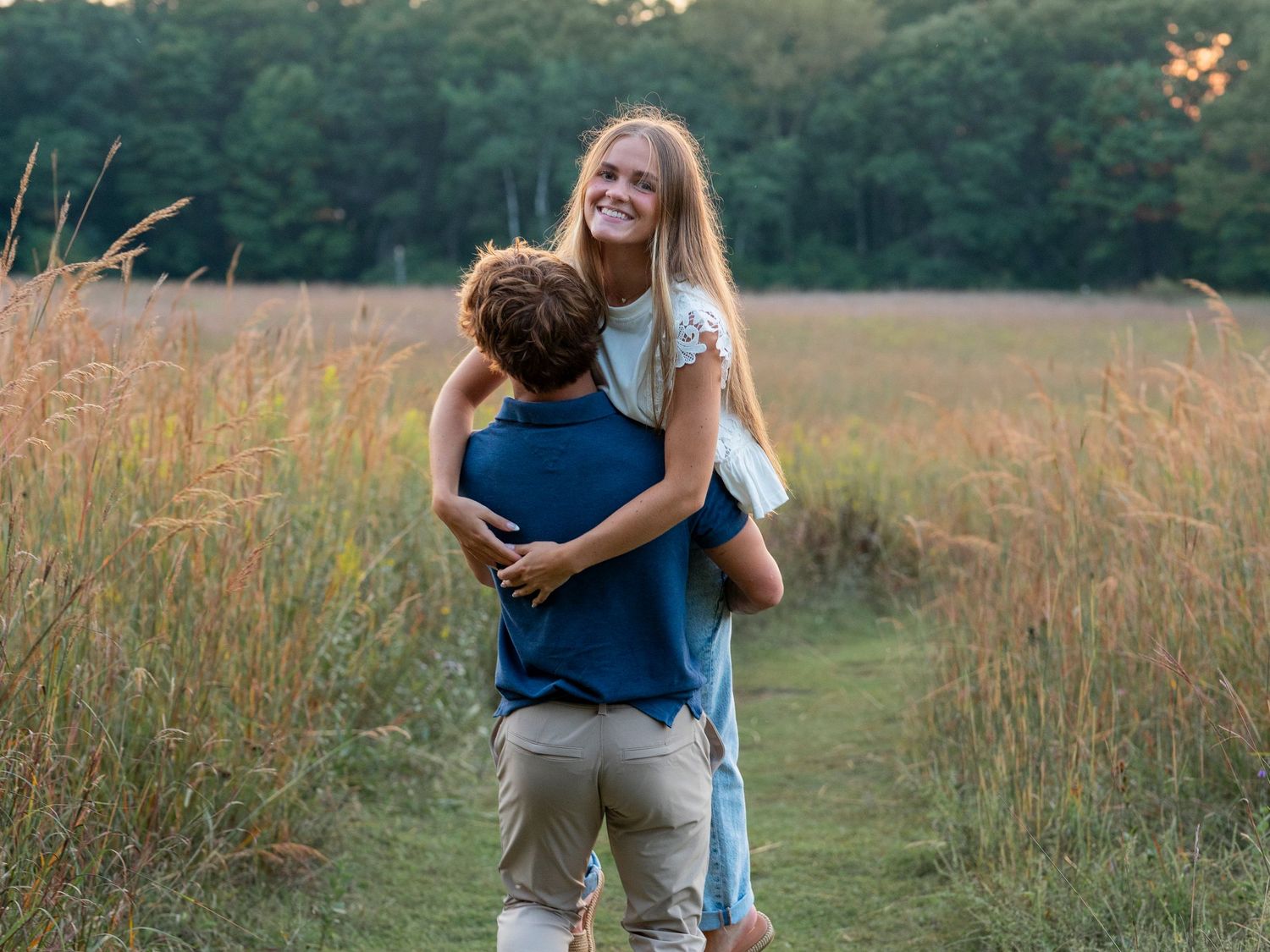 A couple shares a playful embrace in a field with tall grass at sunset.