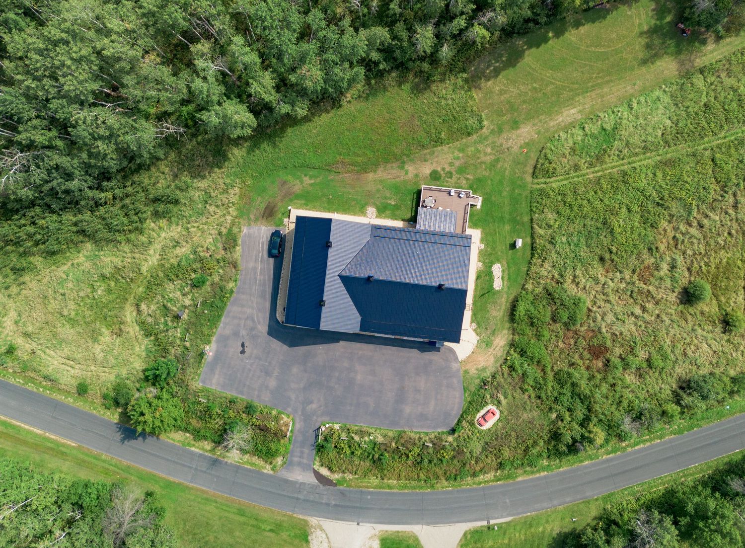 Drone perspective of a building complex nestled in lush green landscape with curved driveways.
