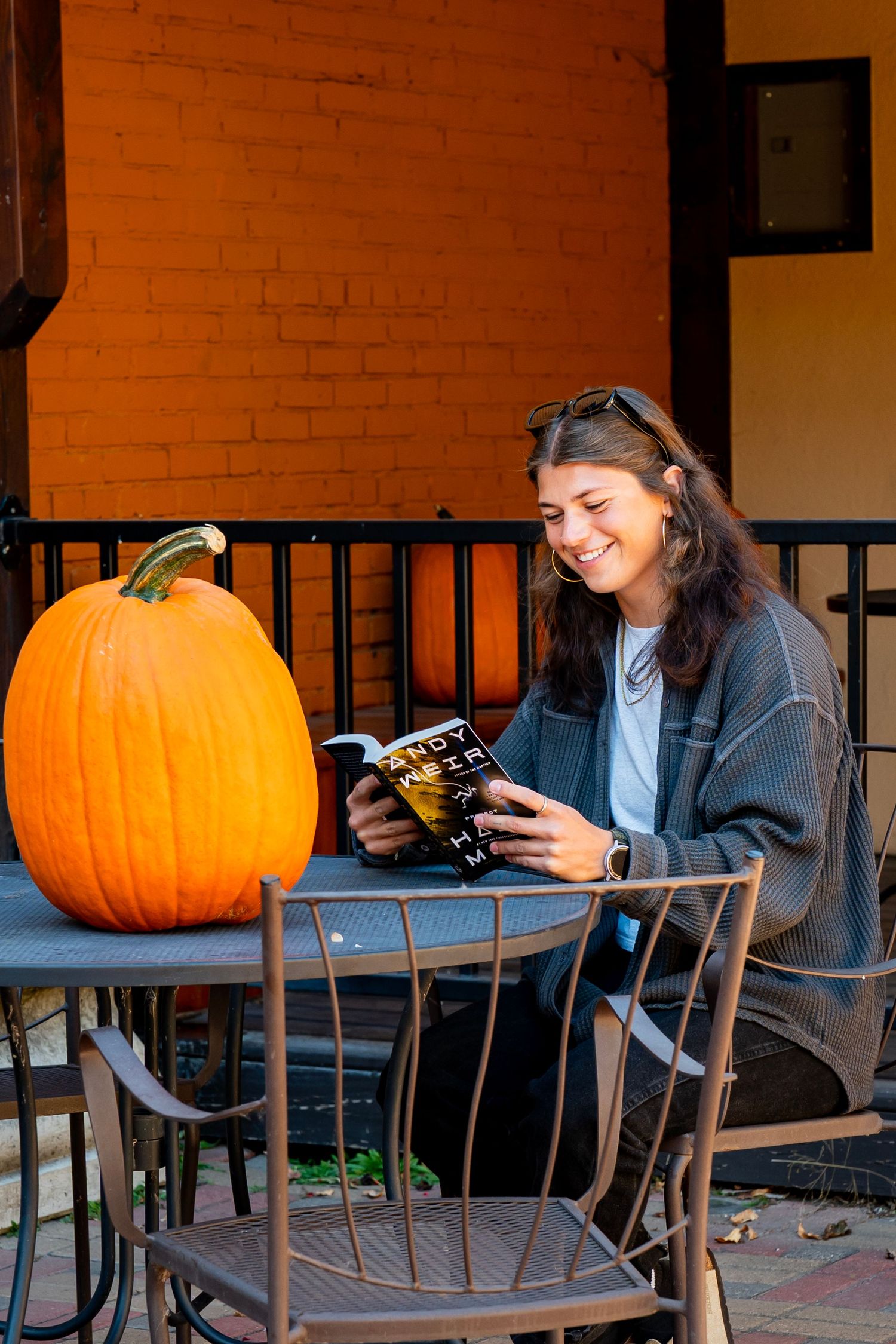 Reading a book at an outdoor cafe in fall with pumpkins and a coffee.