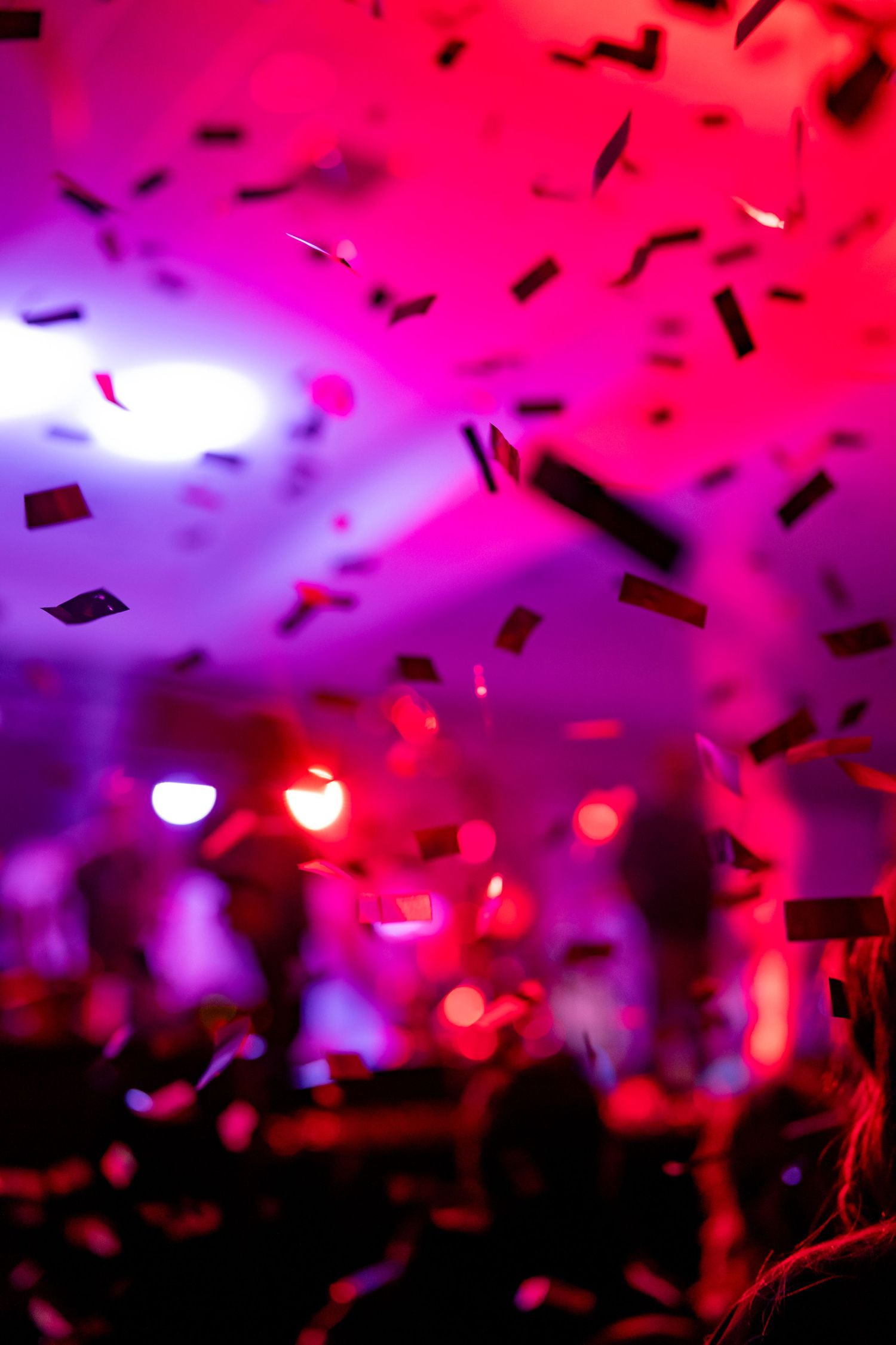 Vibrant pink and purple confetti falling under dramatic concert lighting.