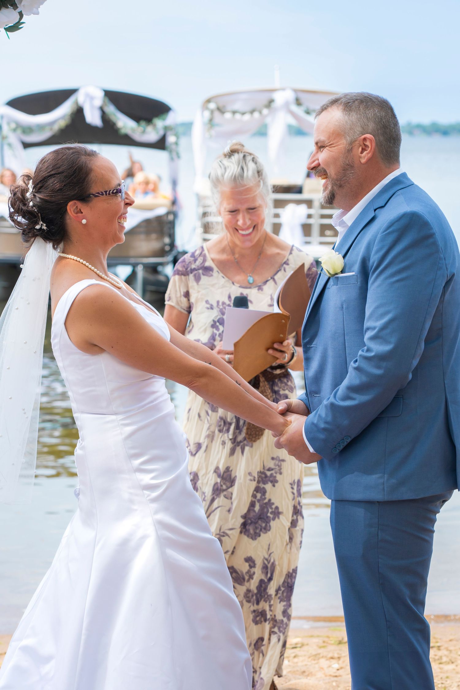 A couple in wedding attire dance together on a dock by the water during their celebration.