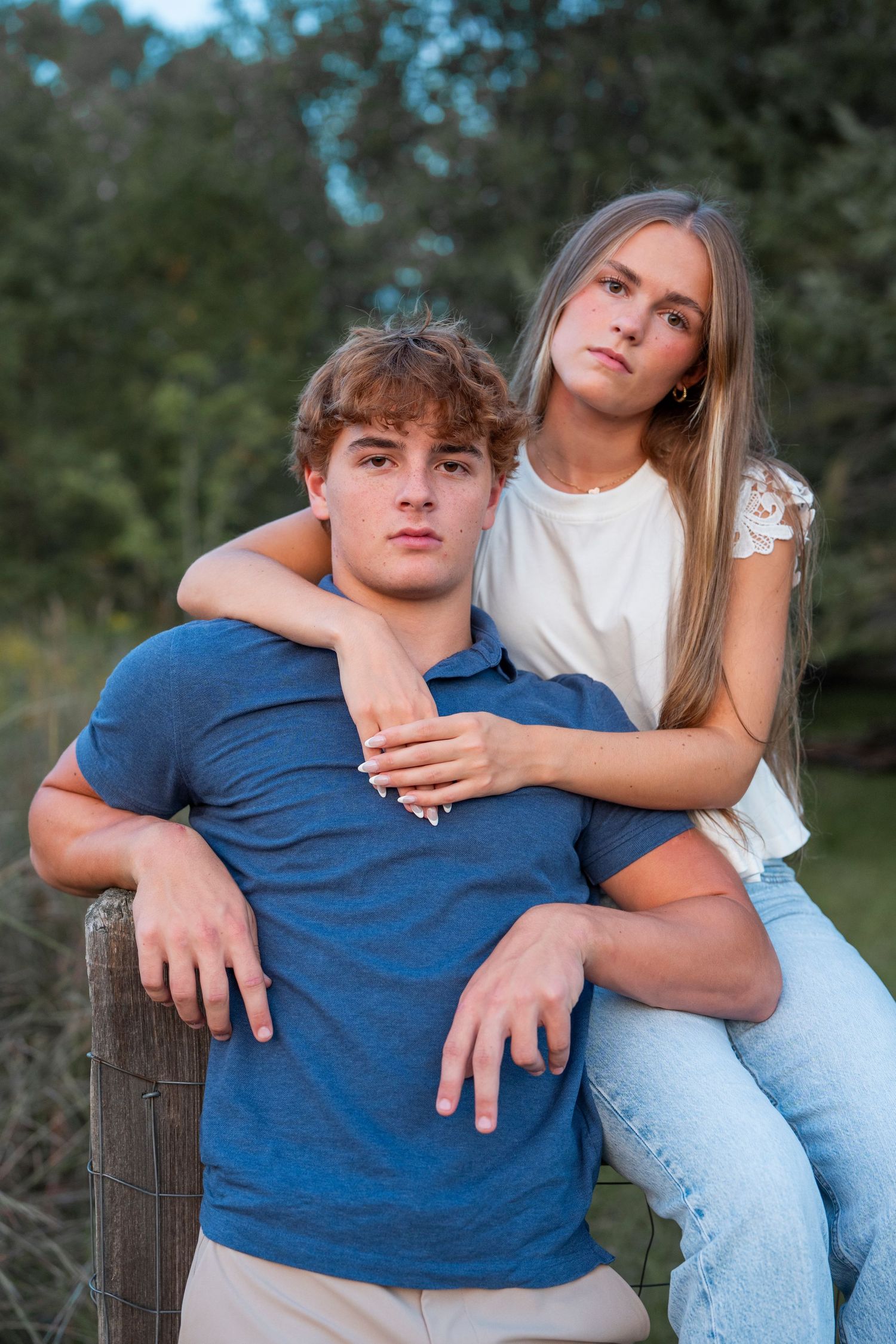 A couple poses together against a rustic fence during an outdoor photoshoot.