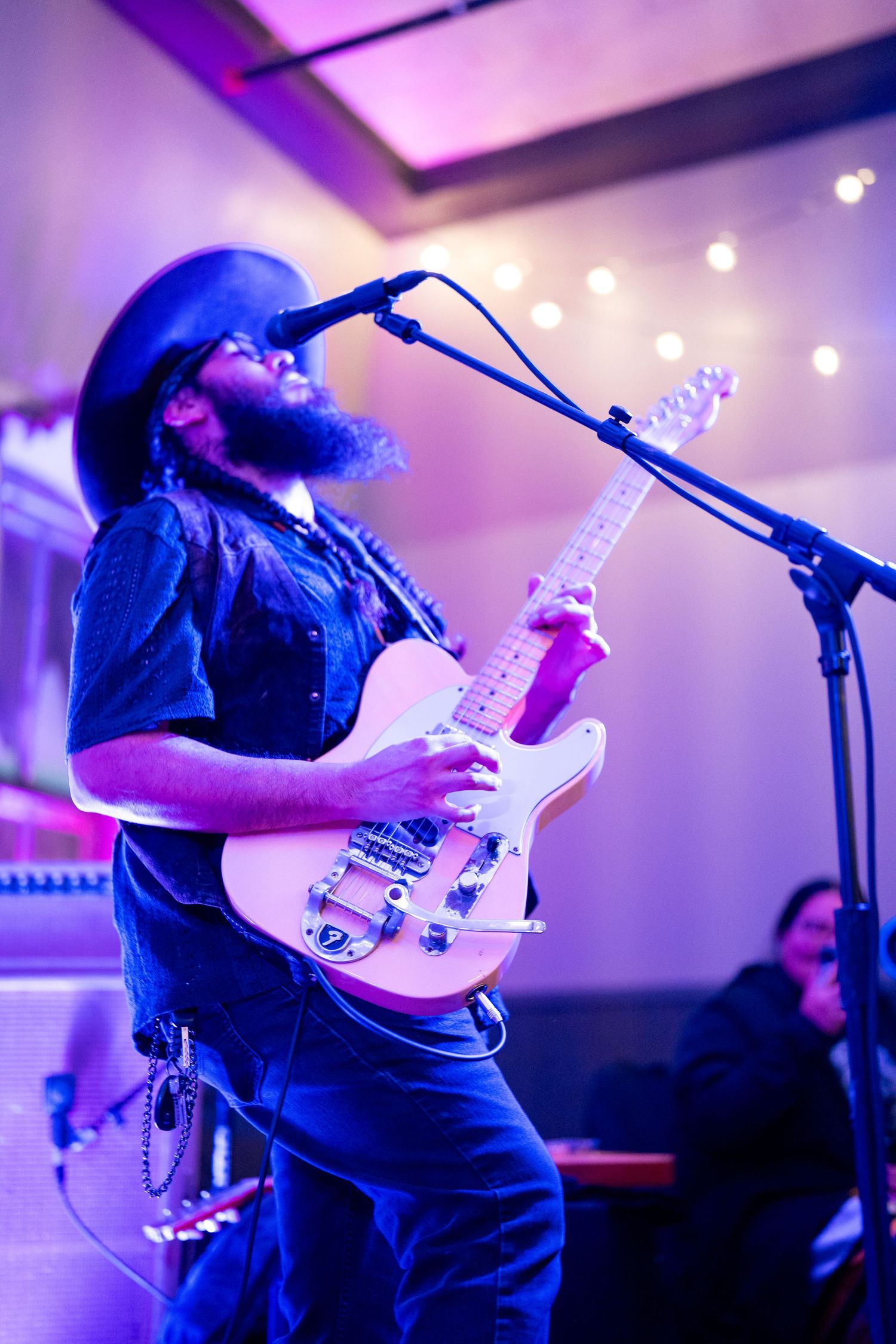 Musician performing with a white bass guitar under purple stage lighting.