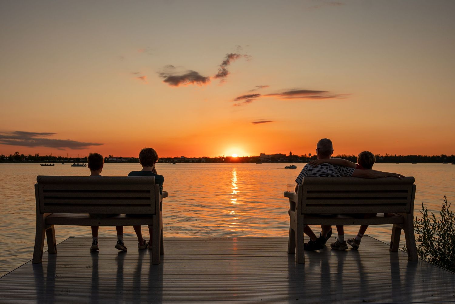 Scenic ocean sunset view with benches silhouetted against an orange sky.