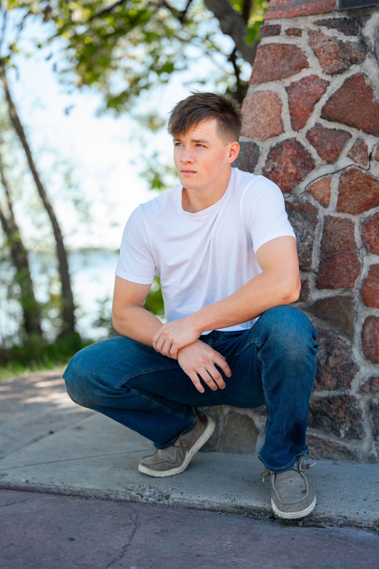 Young man in white t-shirt and jeans crouching by decorative stone wall.
