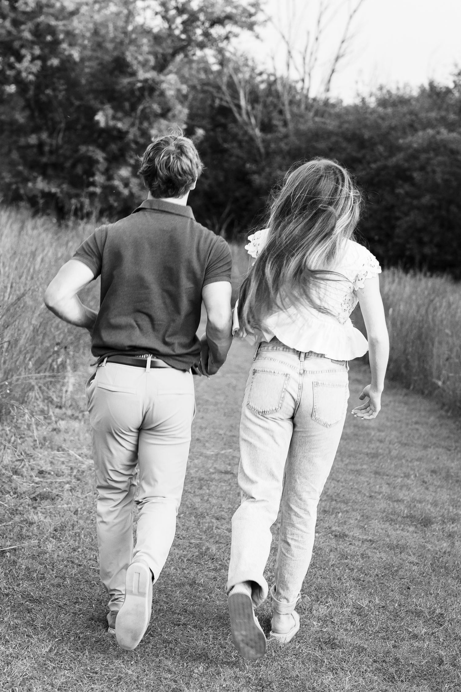 A black and white photo of a couple running together through a grassy field.