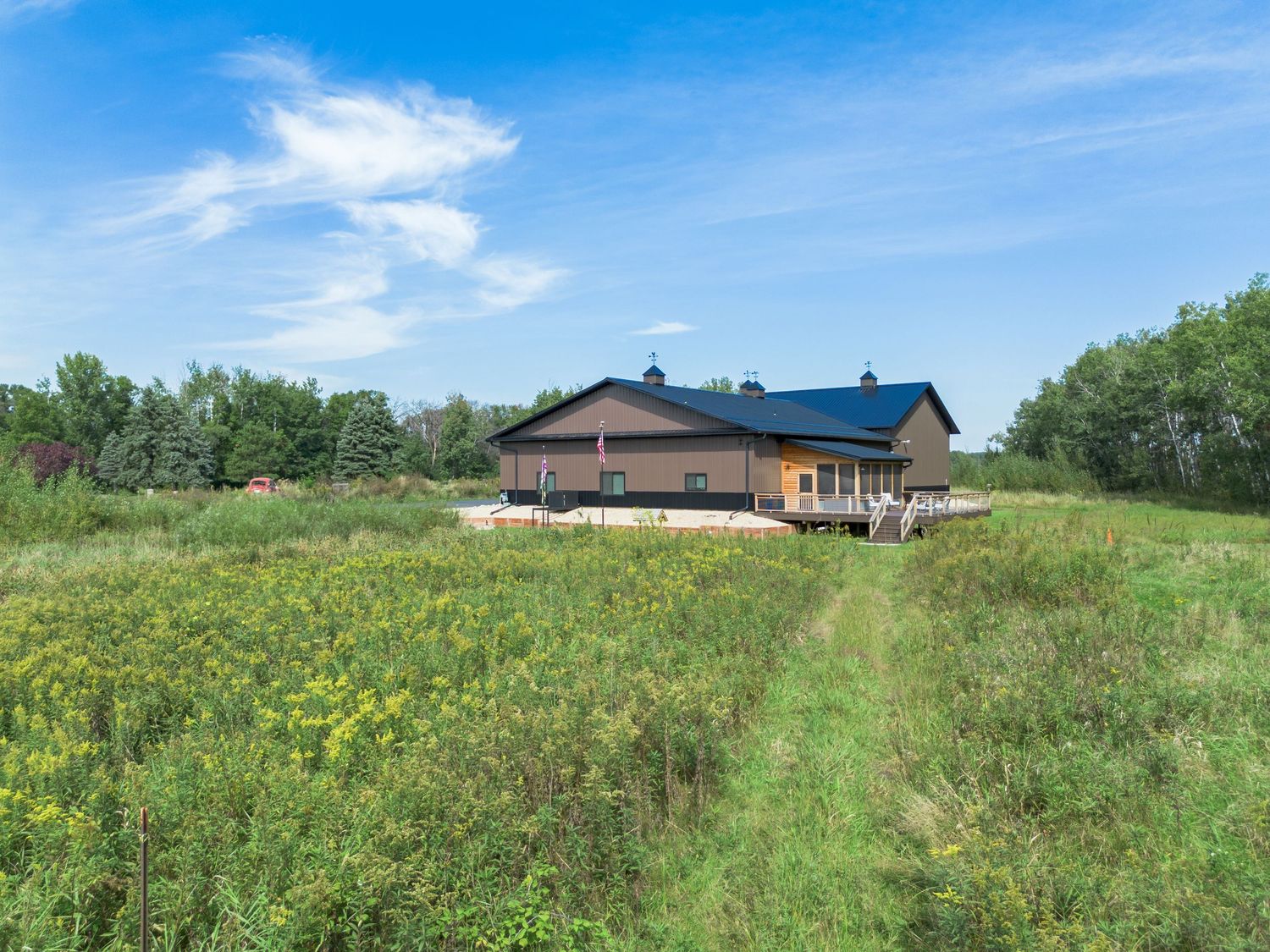 Wide angle shot of rural property with buildings set against lush green meadows and forest backdrop.