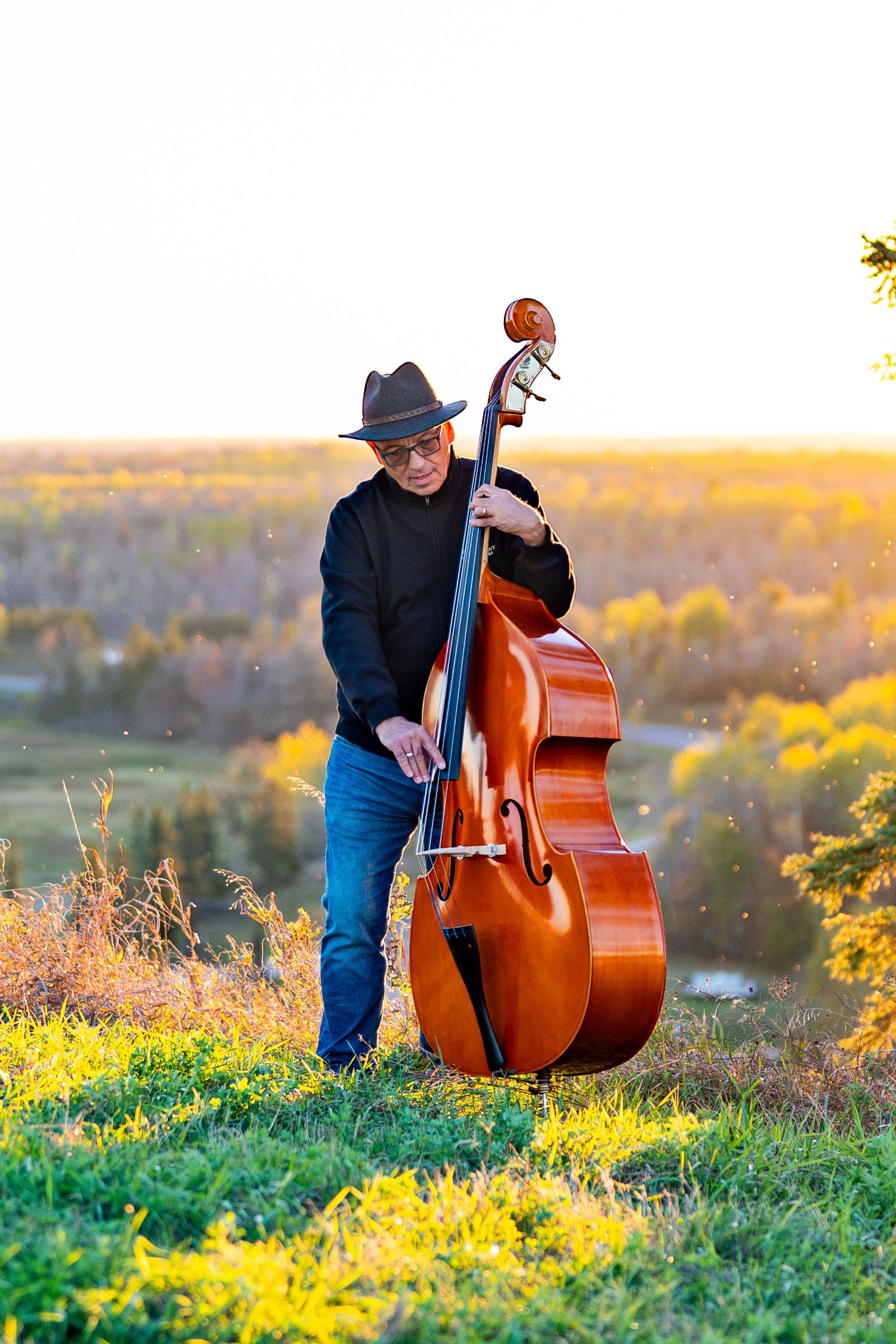Musician playing upright bass outdoors during golden hour.