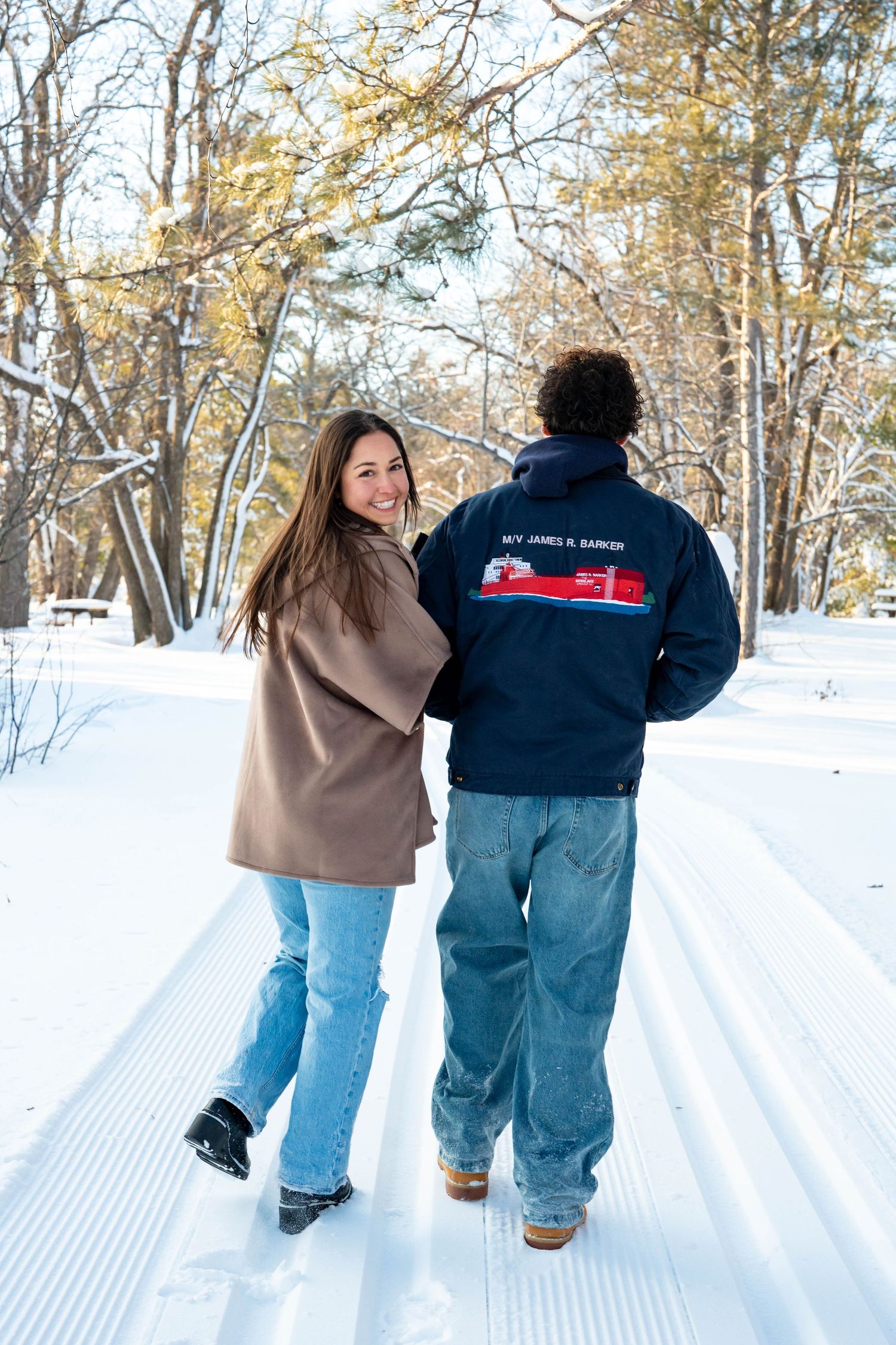 A group of people walking together on a snowy trail through a winter forest landscape.