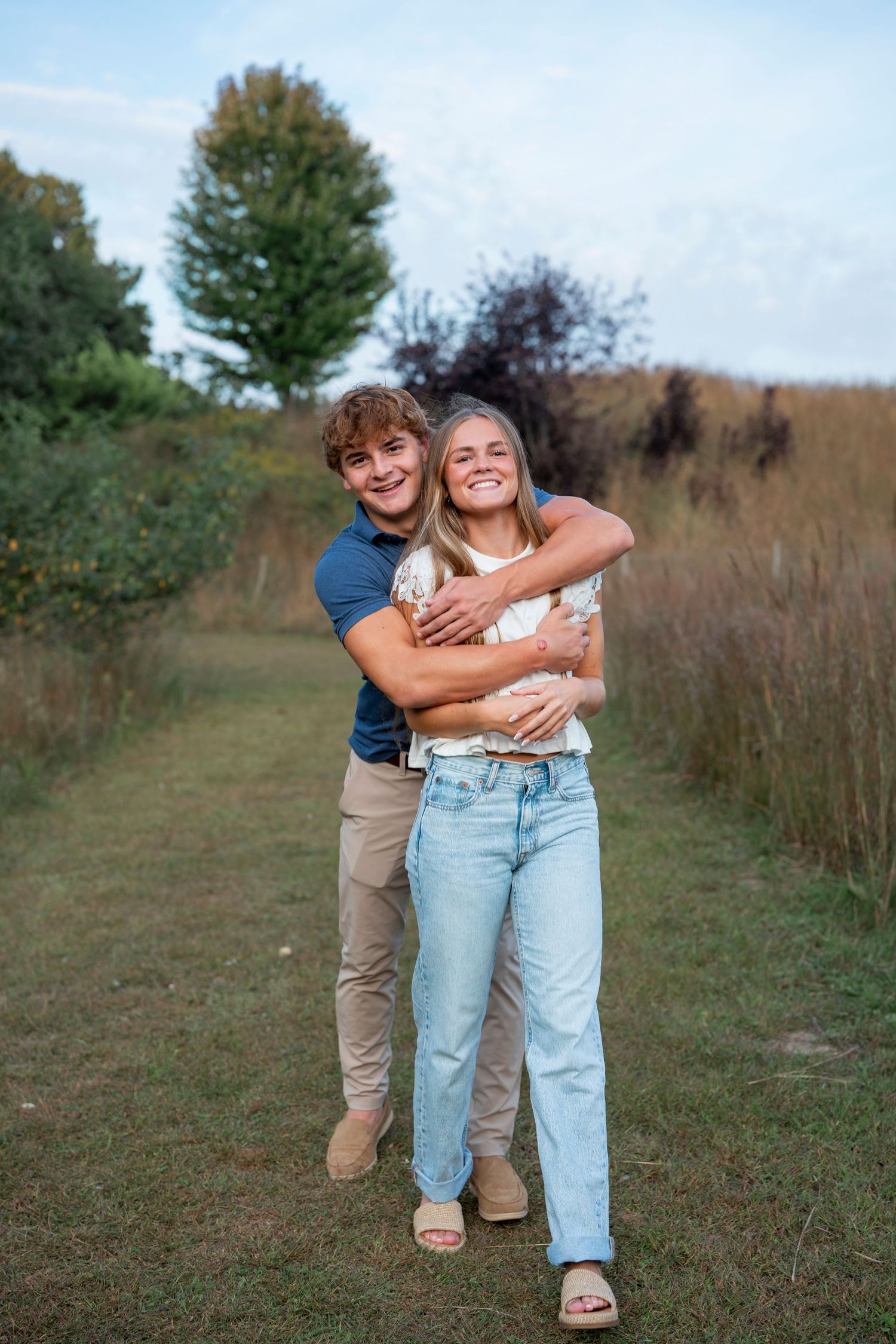 A couple plays and embraces playfully in a sunny outdoor field.