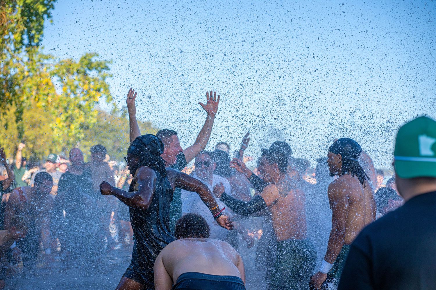 People raising hands in celebration as water sprays through the air after football game.