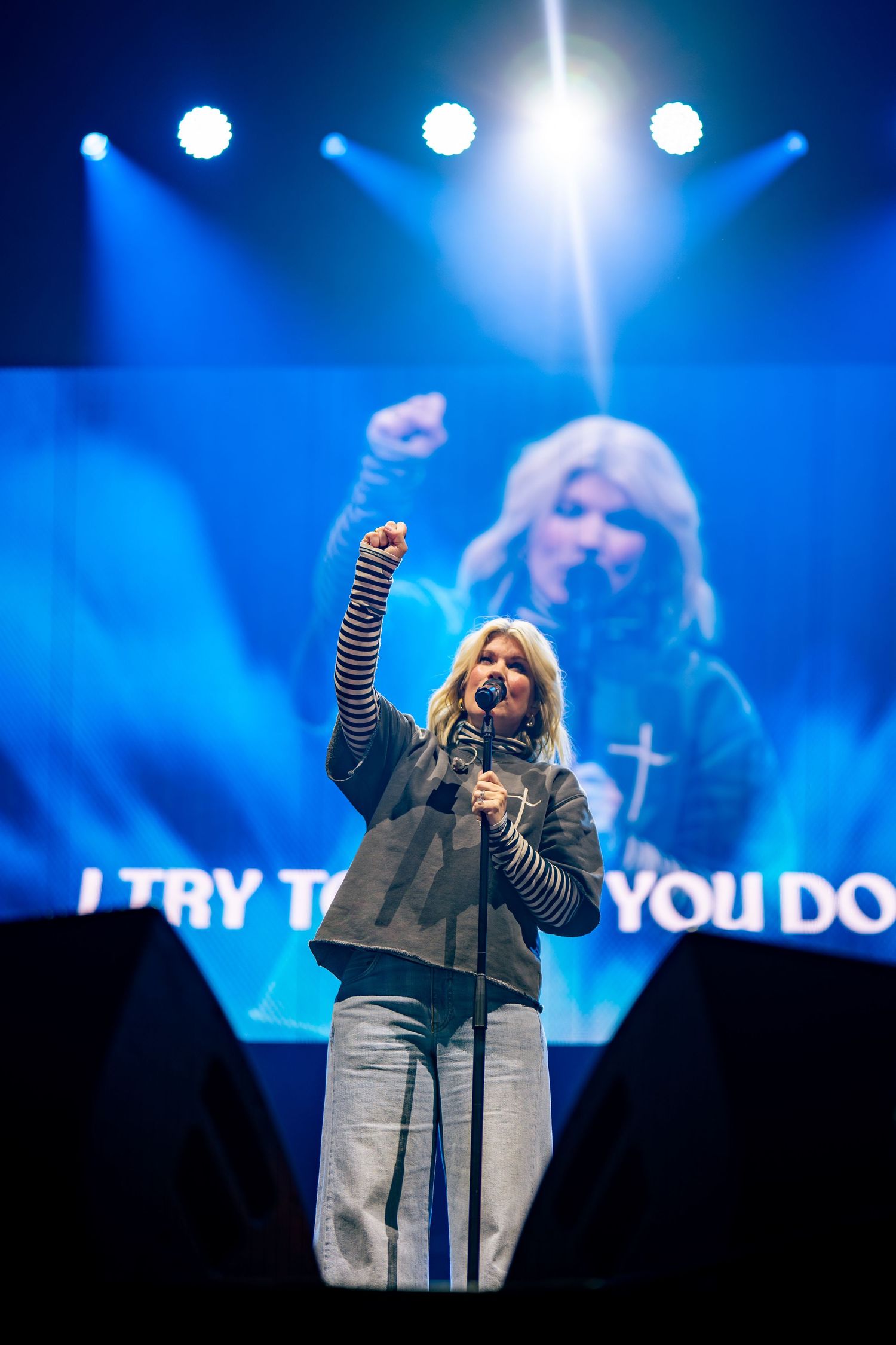 Performer on stage with dramatic blue lighting and spotlights during concert.
