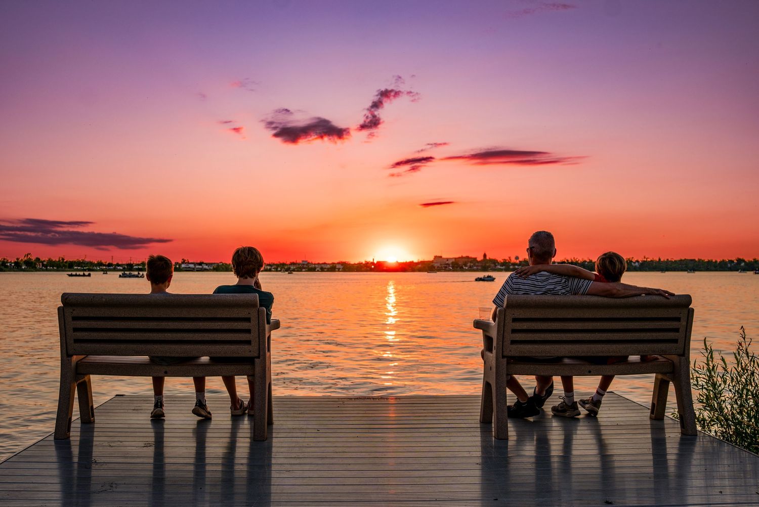 Silhouettes of people on benches watching vibrant orange sunset over Lake Bemidji.
