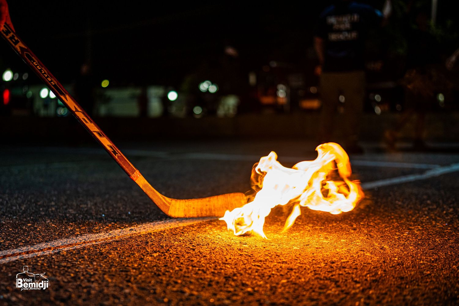 Fire trails behind a unicycle hockey stick on dark asphalt creating dramatic light patterns.