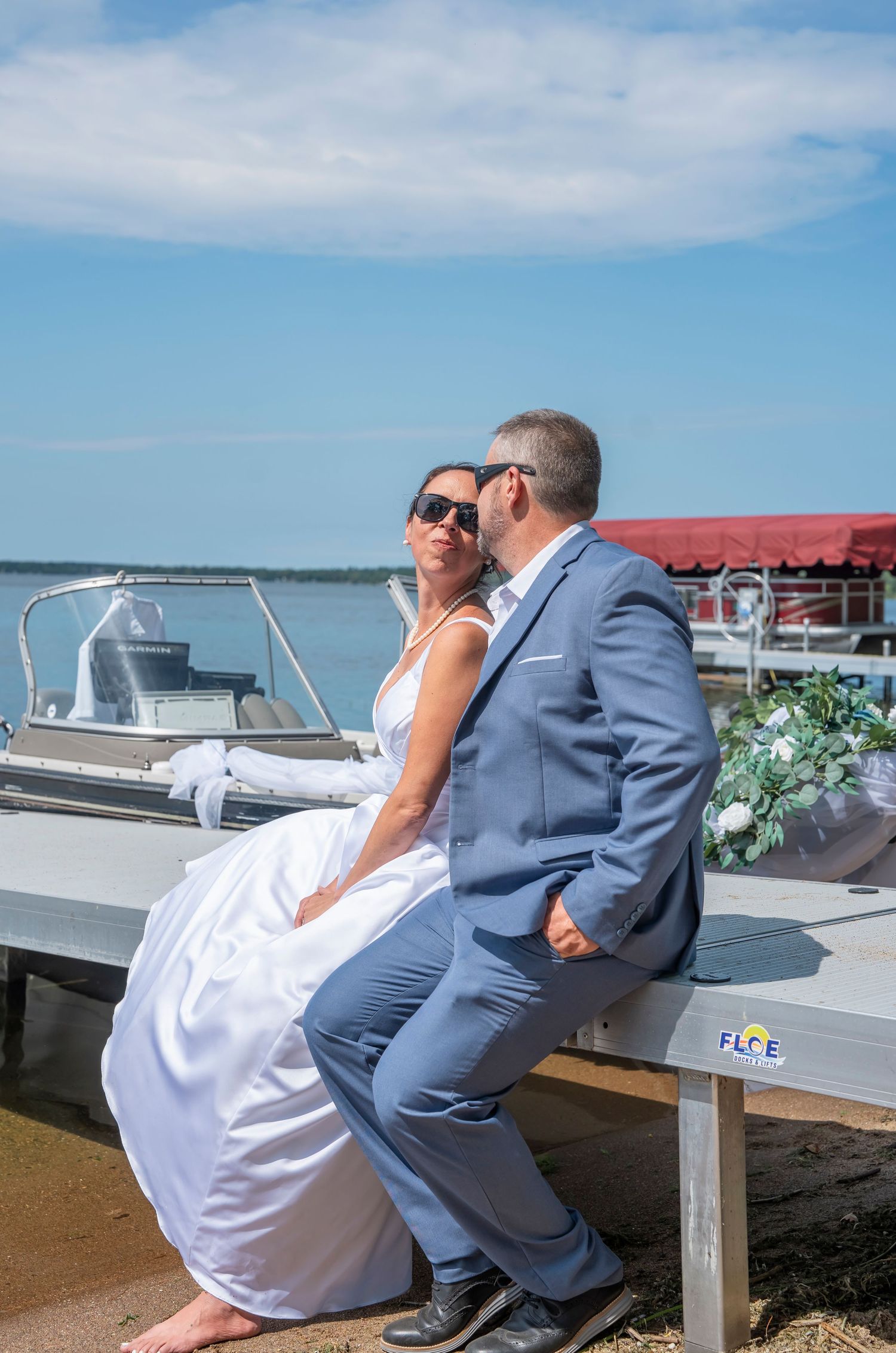 Newlyweds share intimate moment on dock with boats and water views.