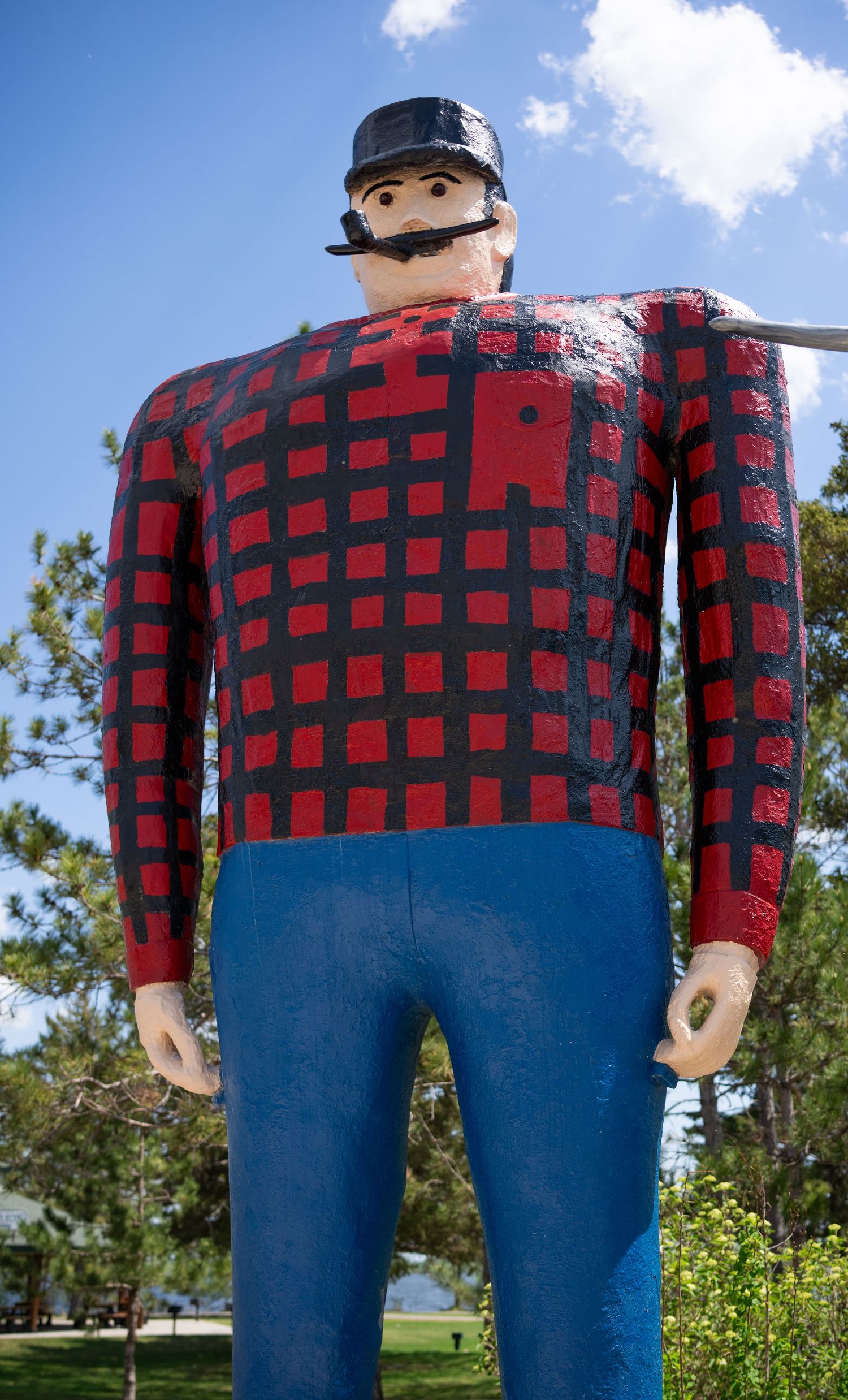 Giant Paul Bunyan statue with red and black plaid shirt and blue pants stands tall against blue sky.