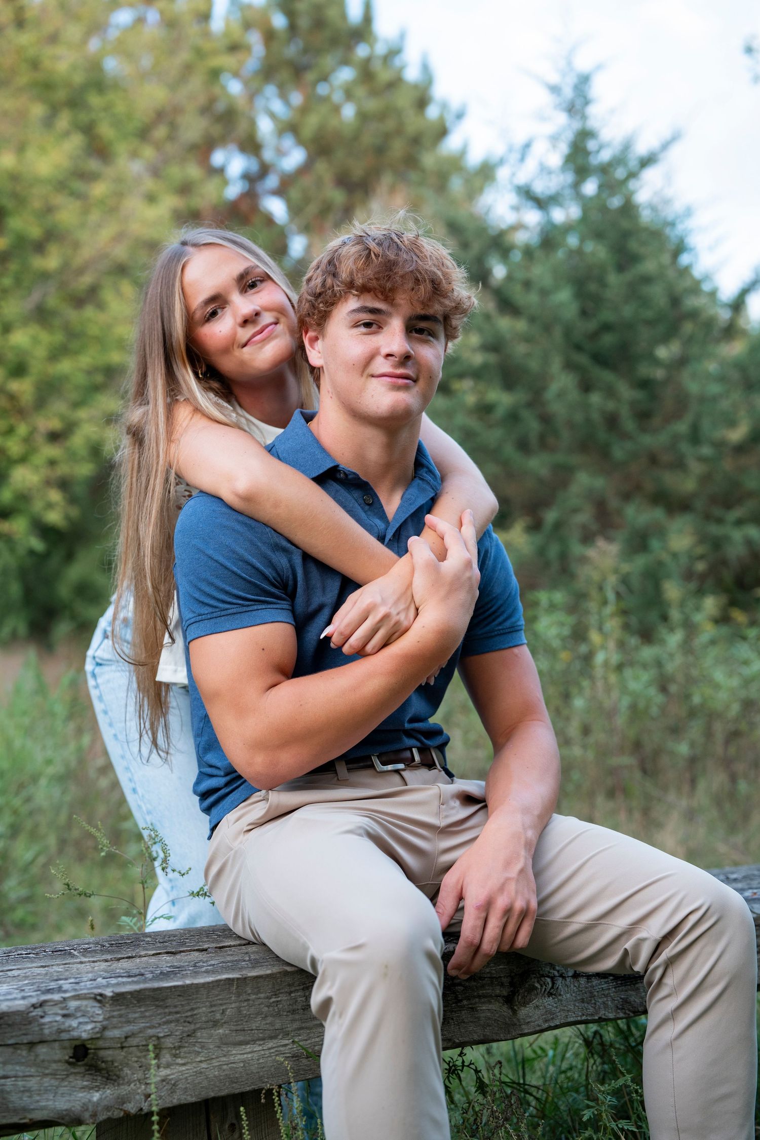 A couple sits together on a wooden log, sharing moments in nature.
