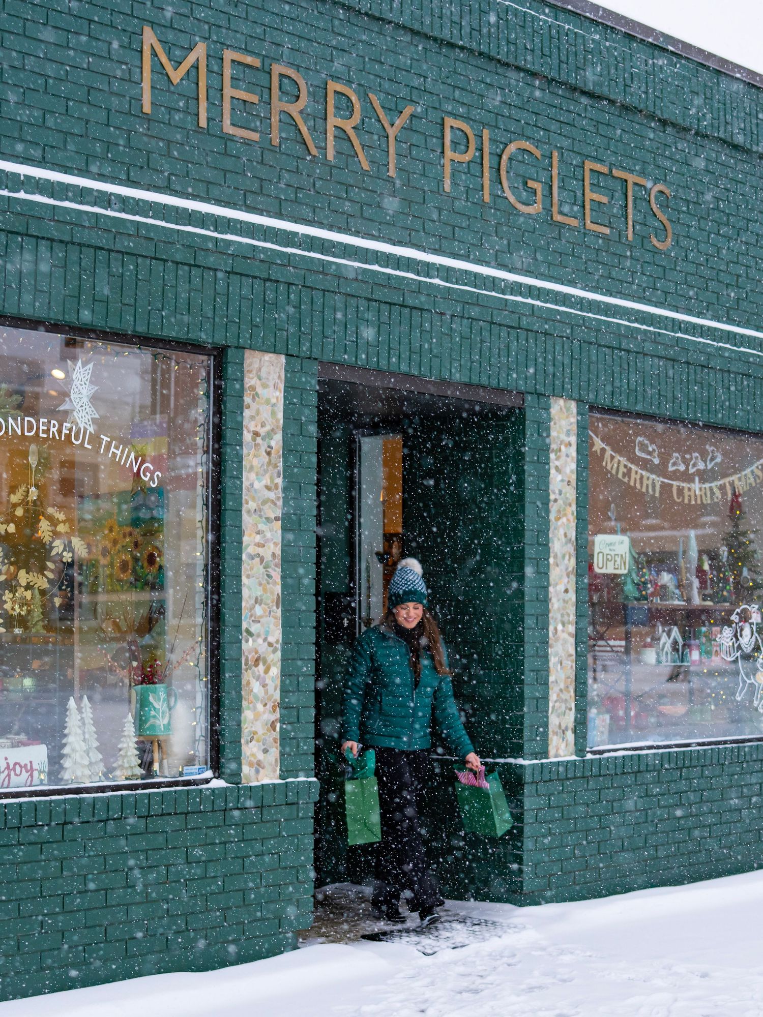 Green brick building 'Merry Piglets' signage in winter snow, downtown shopping in Bemidji.