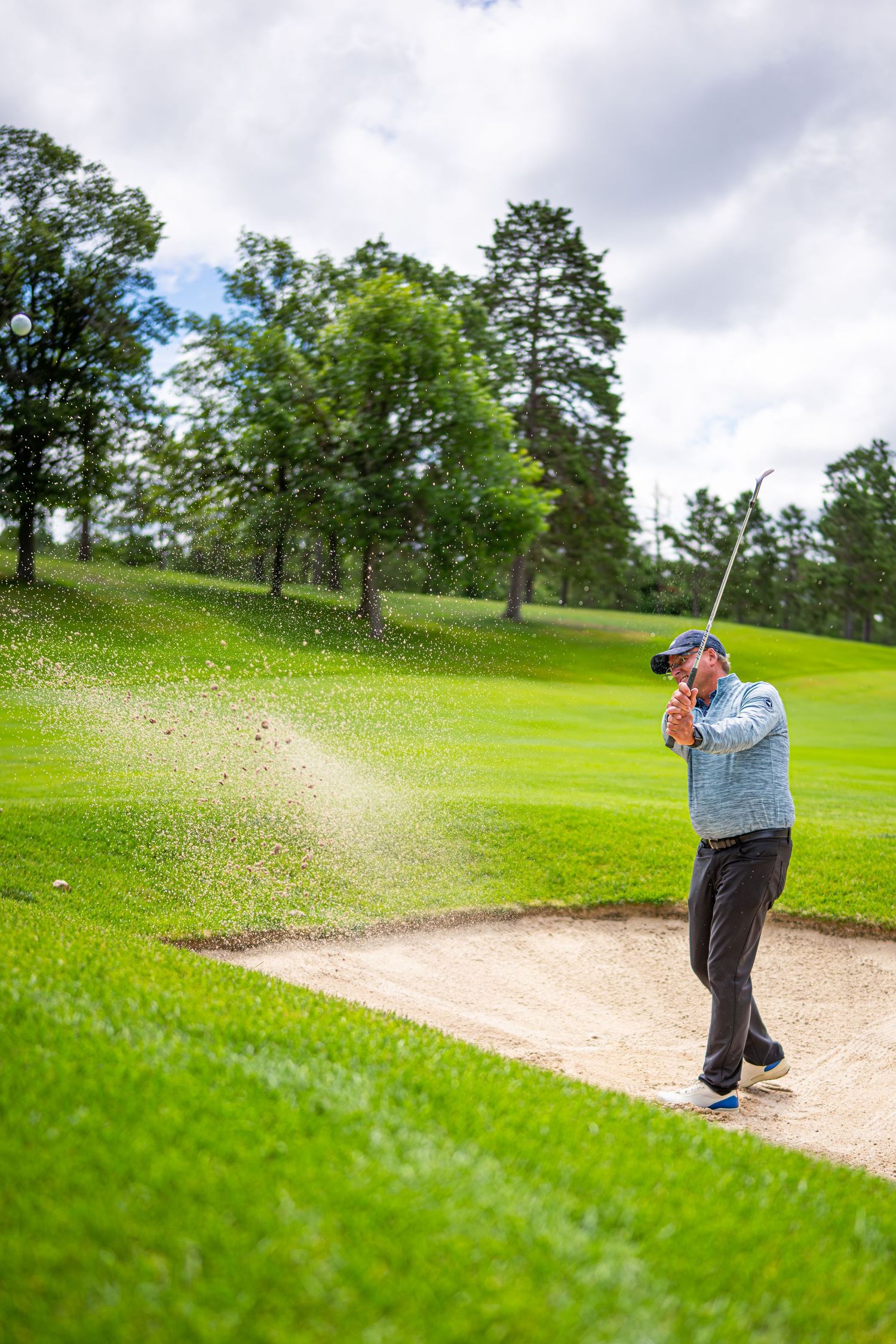 Sand sprays as golfer executes bunker shot on golf course.