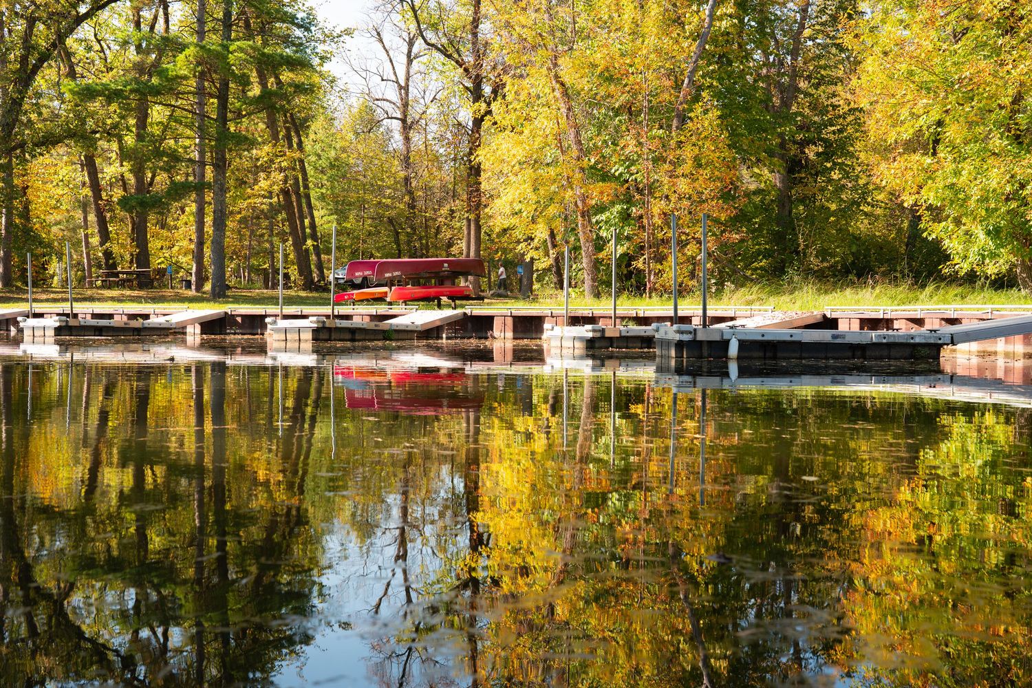 Fall foliage reflects perfectly in still water with wooden docks visible along shoreline.