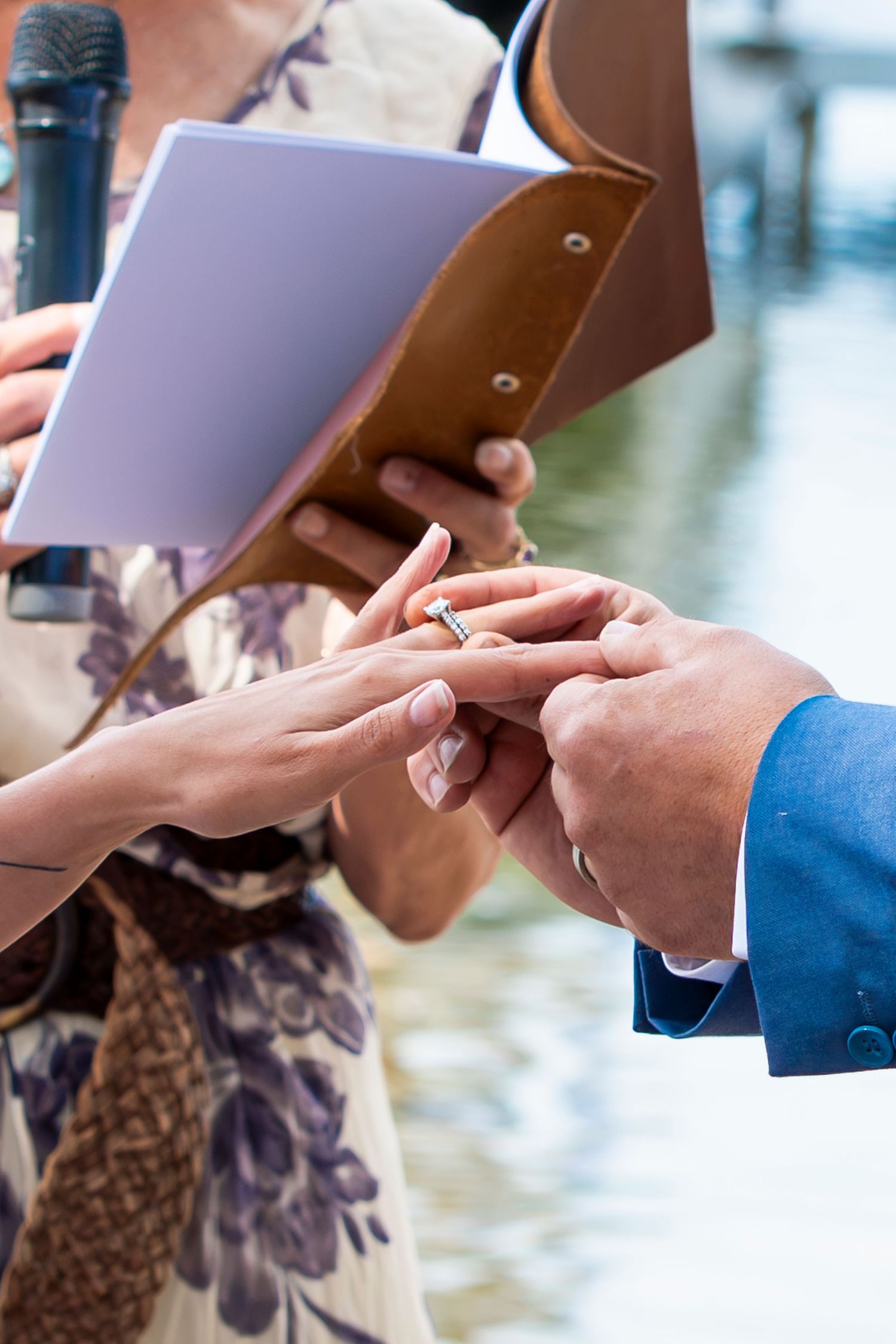 Close-up of hands exchanging wedding vows from paper during outdoor ceremony.