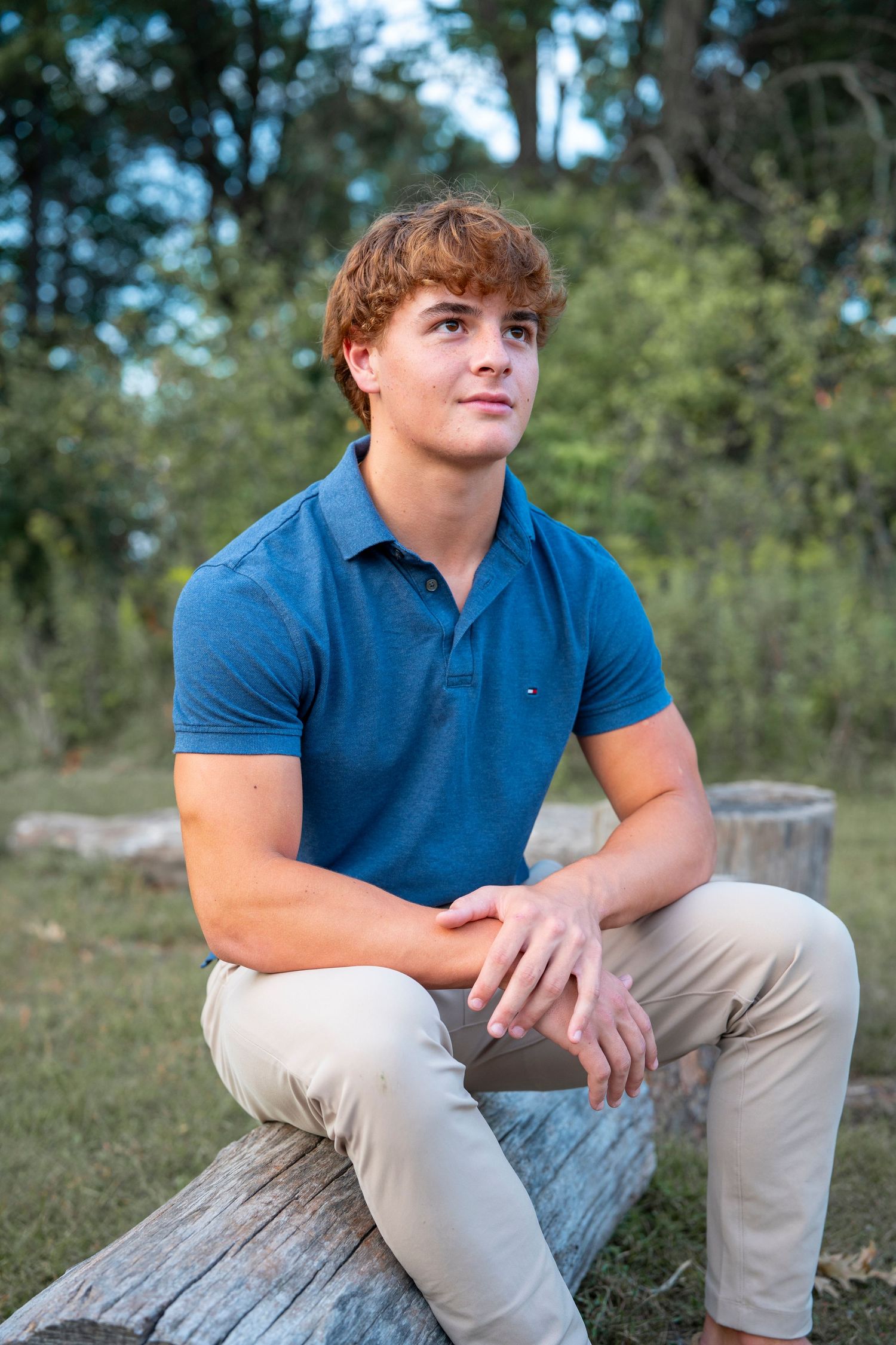 Relaxed outdoor senior portrait session on a fallen log with natural greenery backdrop.