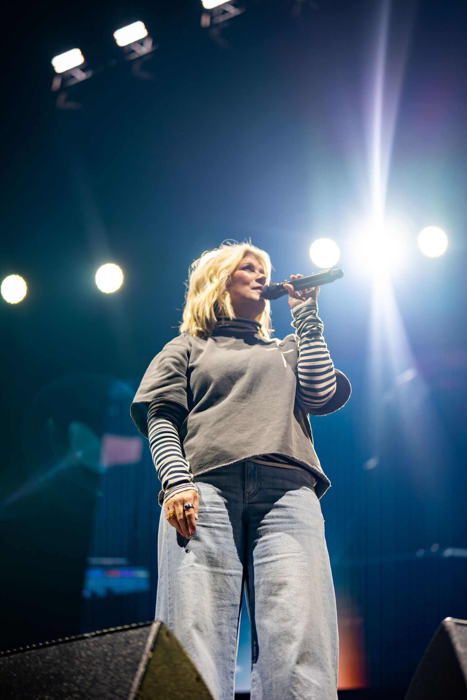 Concert performer in casual outfit singing under bright stage lights.
