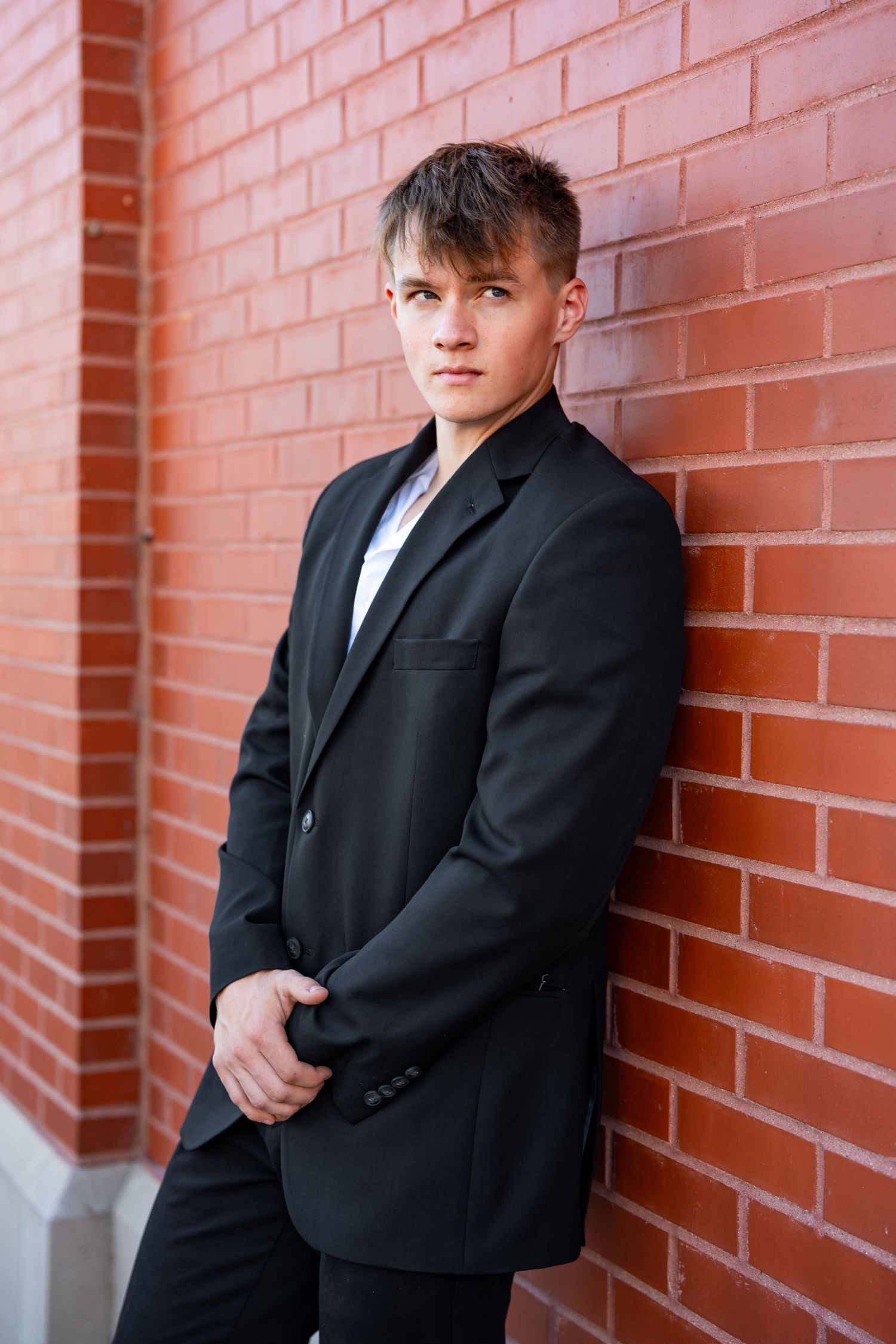Multiple poses of a person in a black suit jacket leaning against a brick wall.