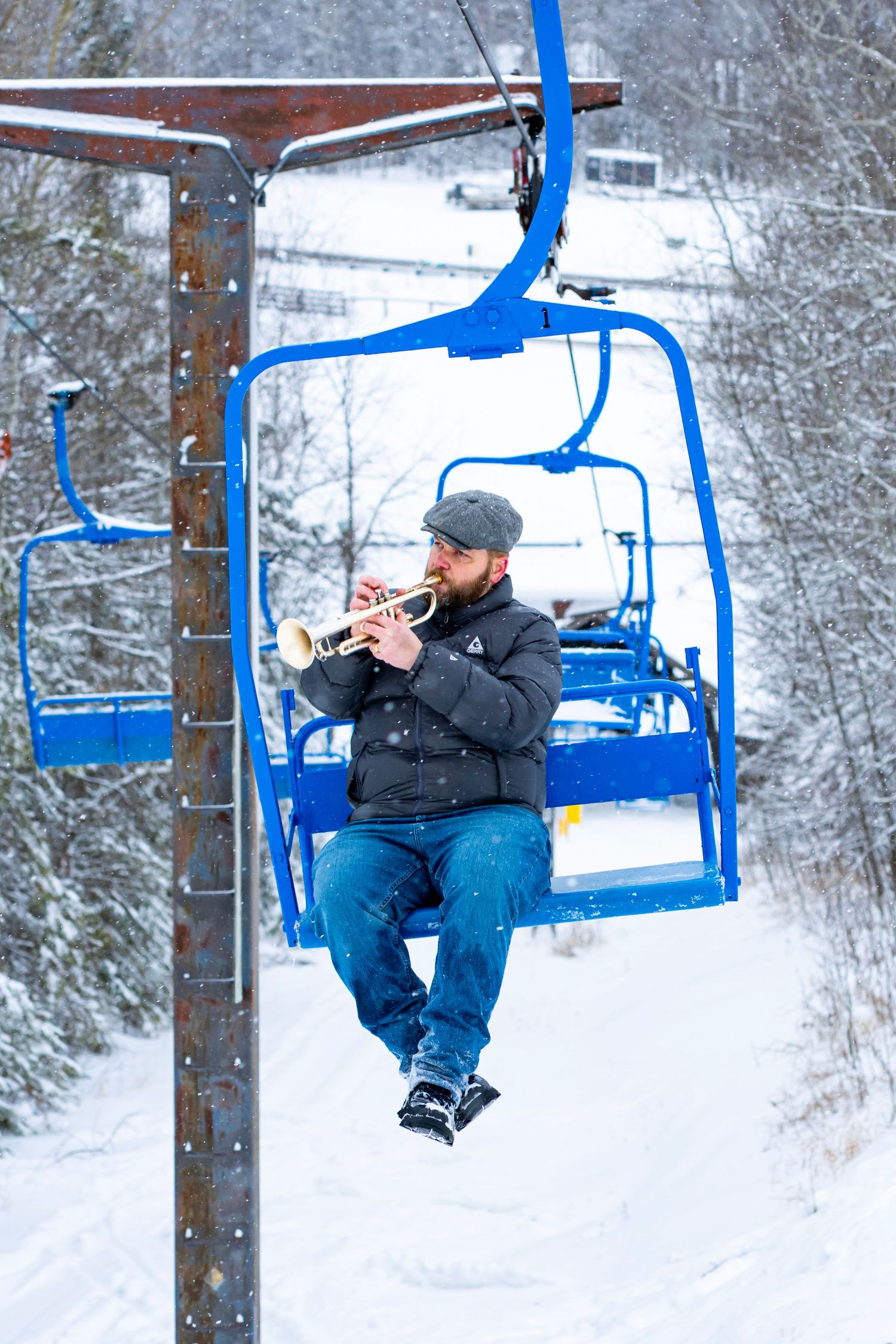 Person riding a blue ski lift chair over a snowy winter landscape.
