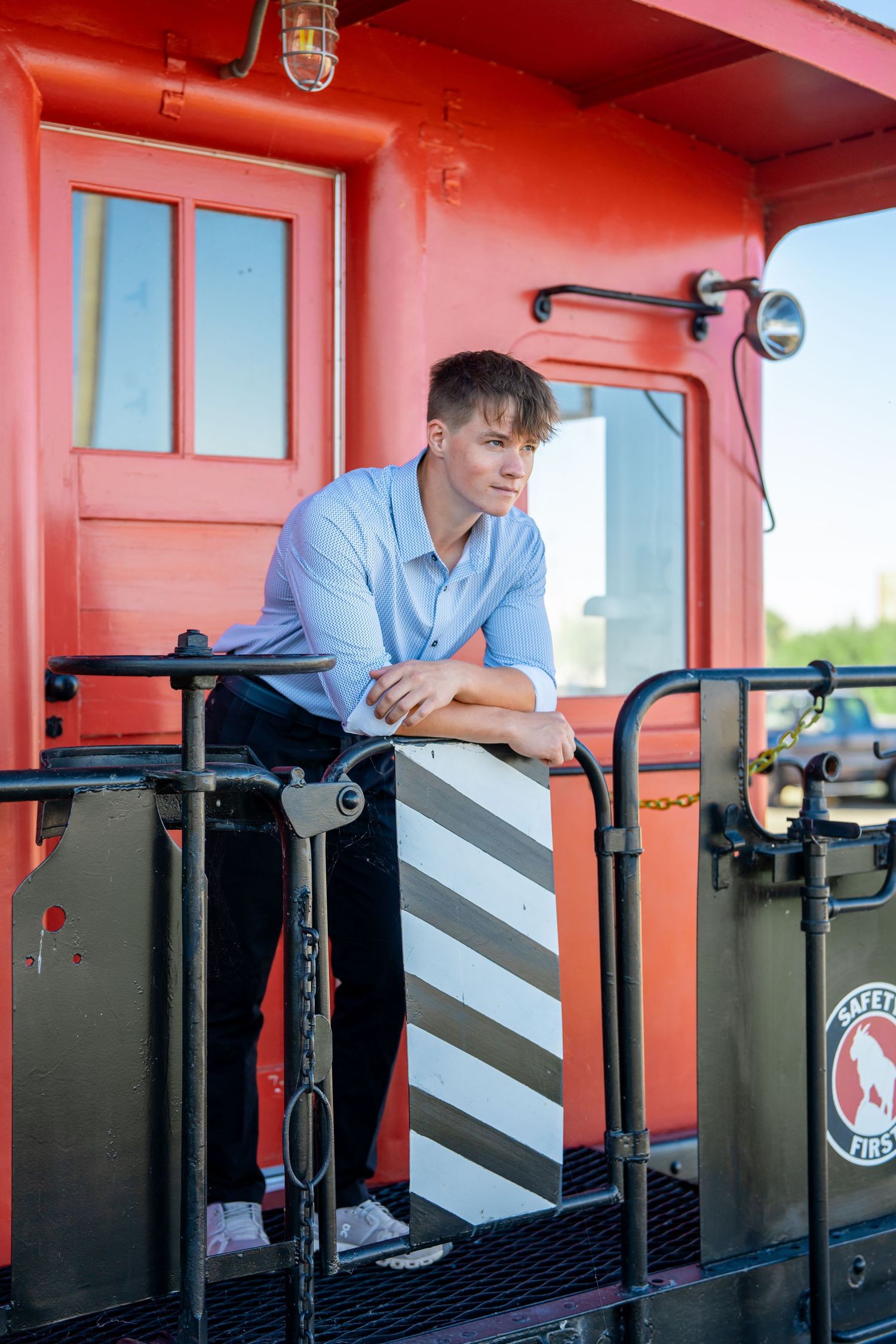 A casual pose on red painted train car platform wearing light blue shirt.